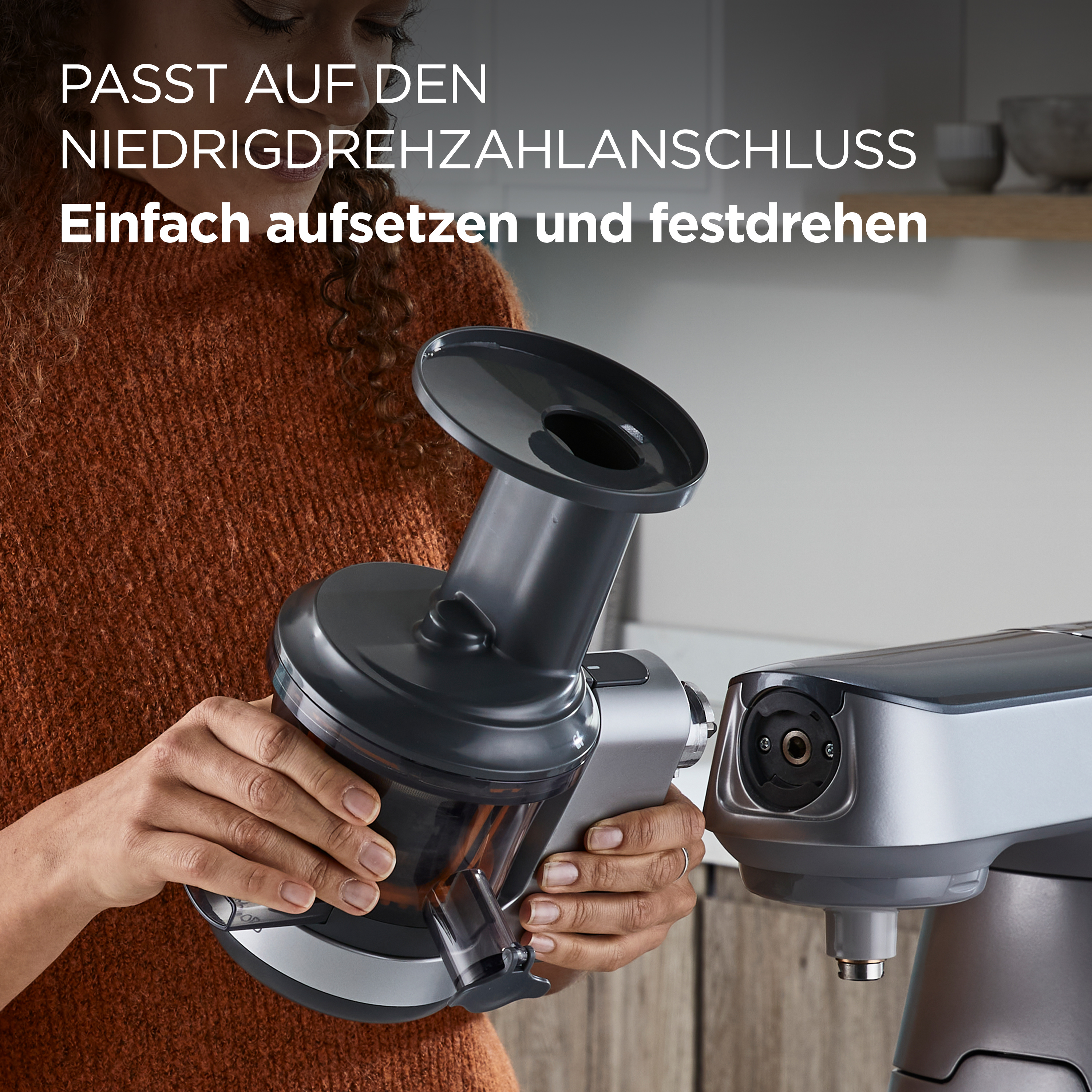 Eine Frau befestigt einen dunkelgrauen Entsafter an einer silbernen Küchenmaschine. Text auf Deutsch.