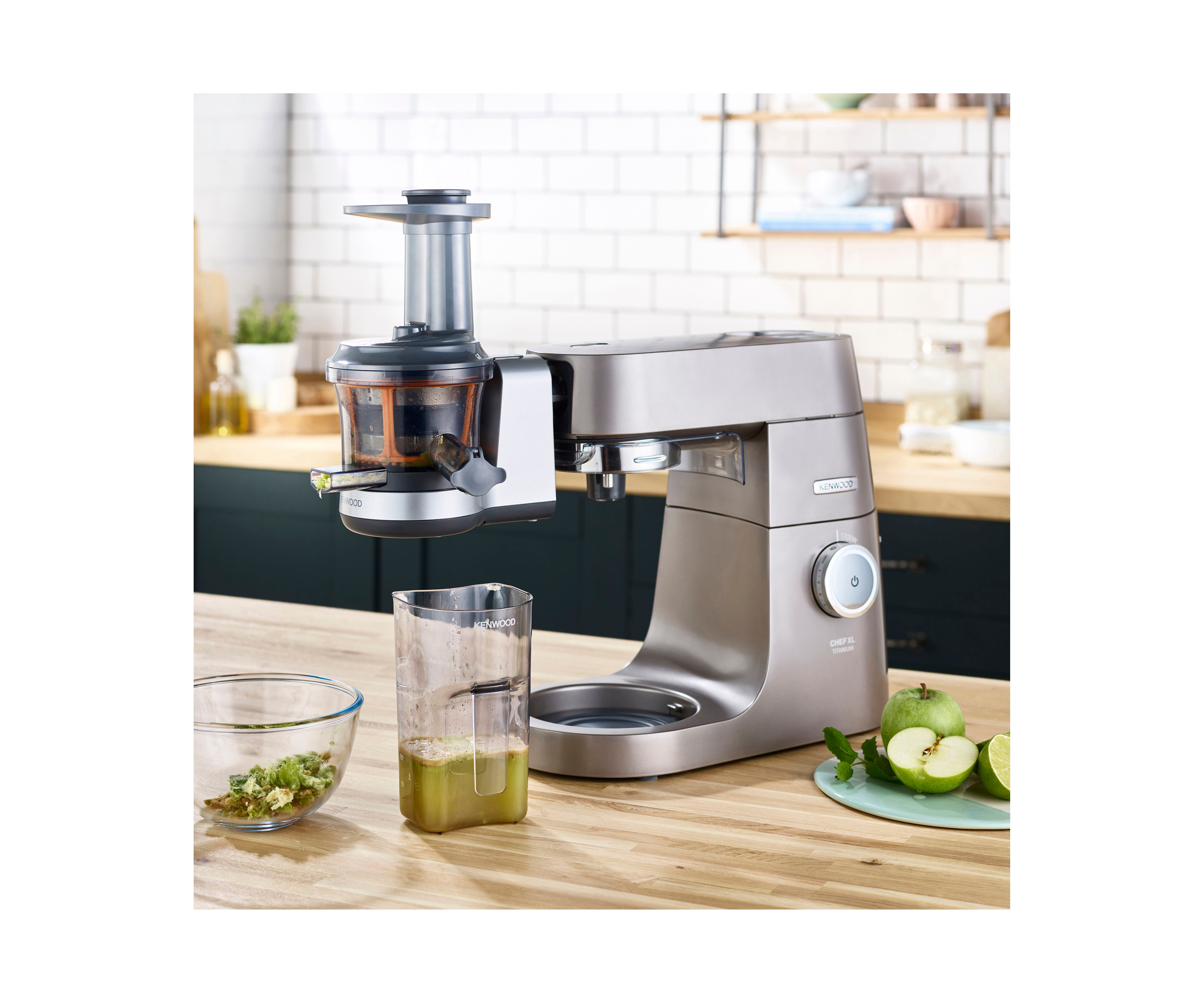 Entsafter und Mixer auf der Holztheke. Apfelscheiben, Saft im Glas und eine Schüssel mit gehacktem Grün.