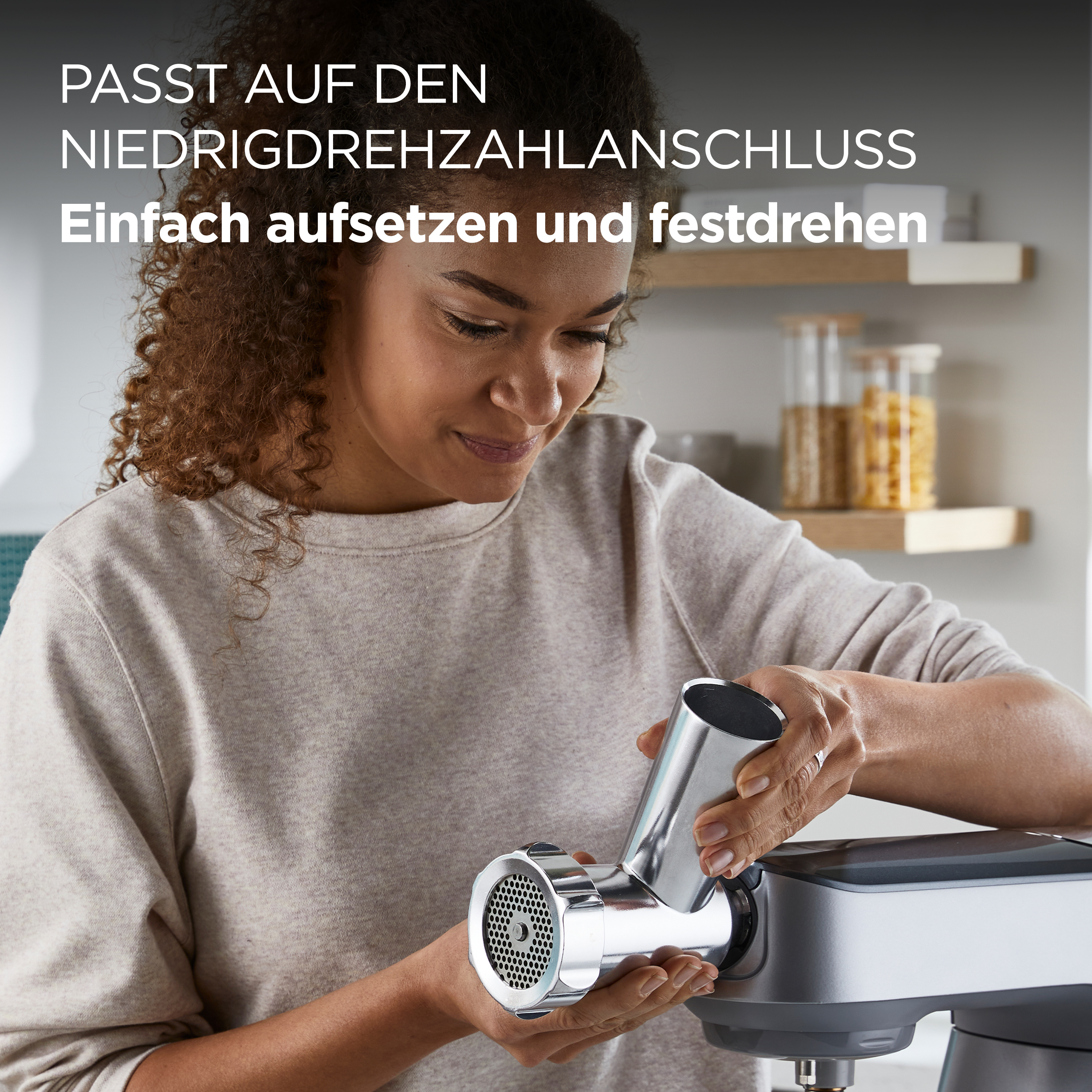 Frau befestigt einen Fleischwolfaufsatz an einem Küchengerät. Text auf Deutsch oben.