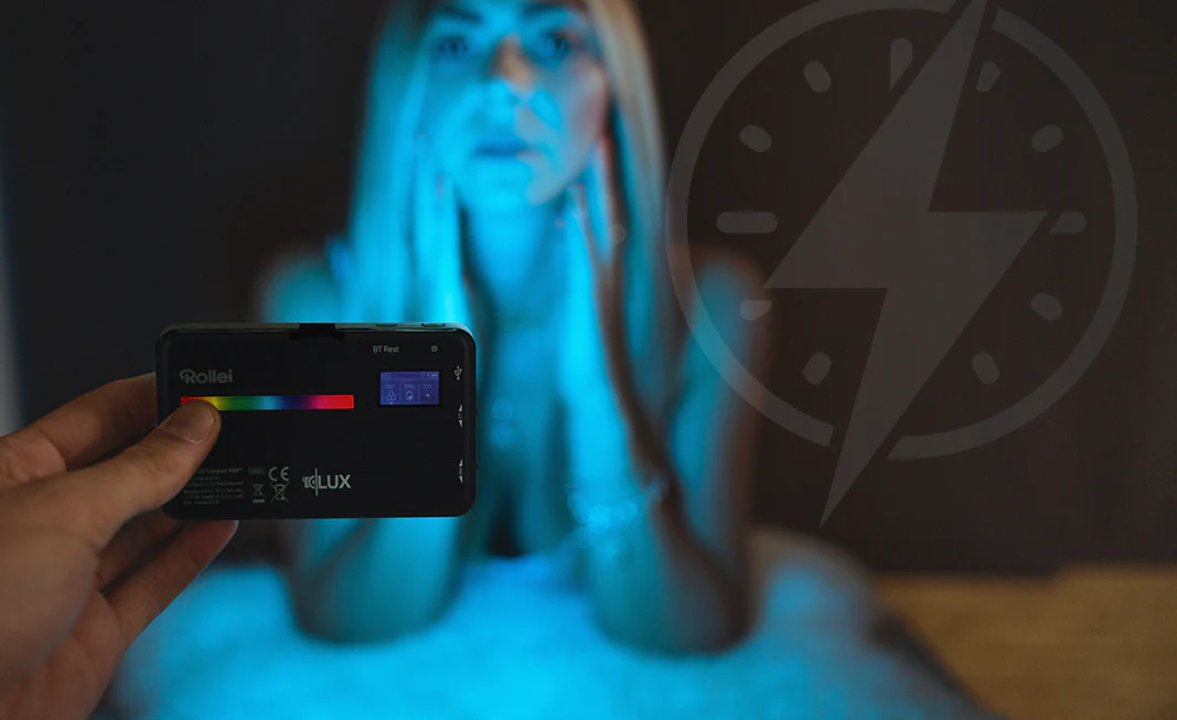 Une main tenant un appareil noir avec des lumières colorées, femme floue en arrière-plan.