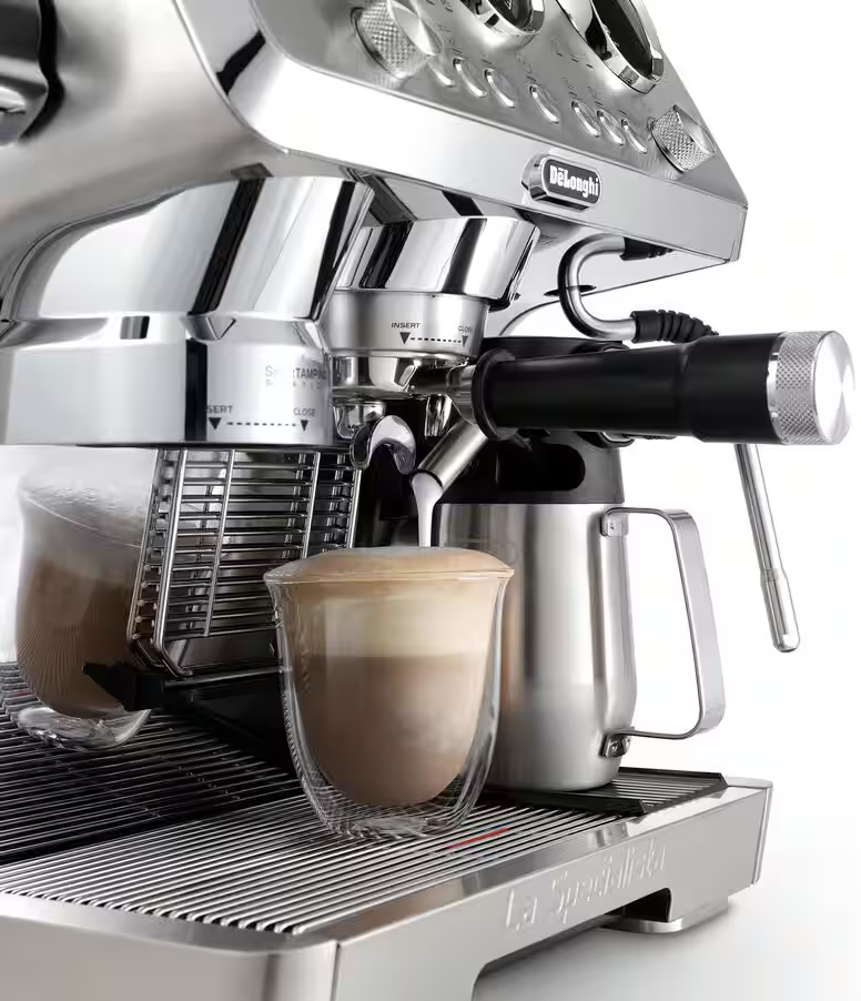 Eine silberne Espressomaschine mit einem Glas Kaffeetasse und einem Milchaufschäumer daneben.