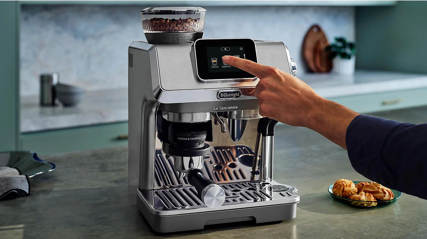 Macchina per caffè espresso argentata con mano che tocca il touchscreen. Sul bancone della cucina.