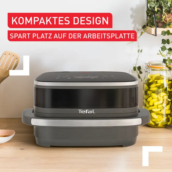 Ein grauer Airfryer auf einem Holztisch, mit deutschem Text.