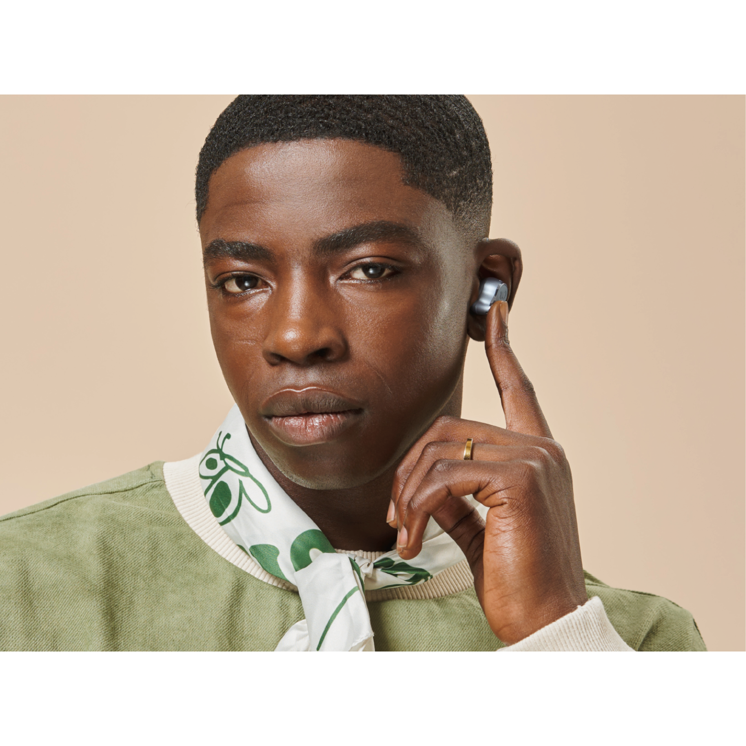 A man wearing an earbud in one ear. He is wearing a green jacket and looking at the camera.