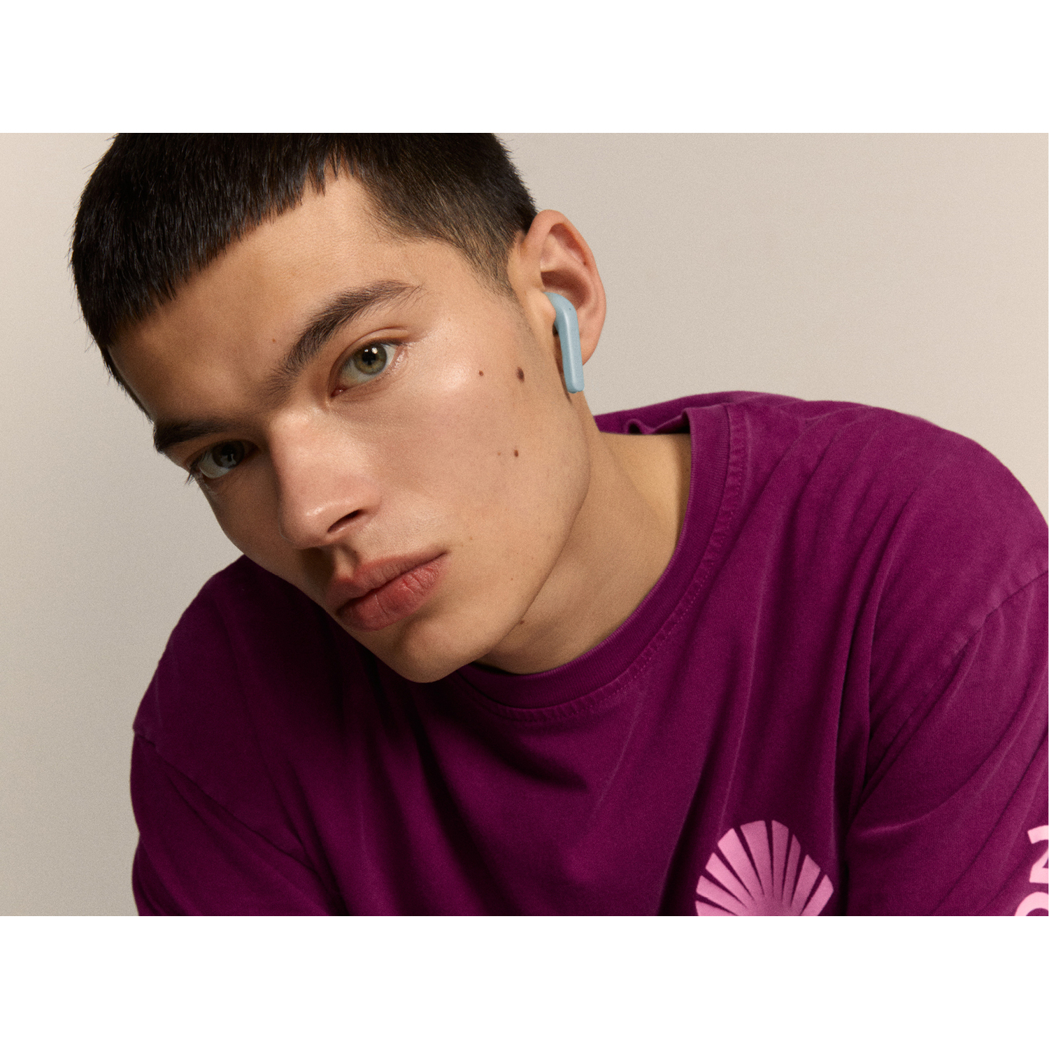Man wearing a purple shirt with one earbud in his ear.