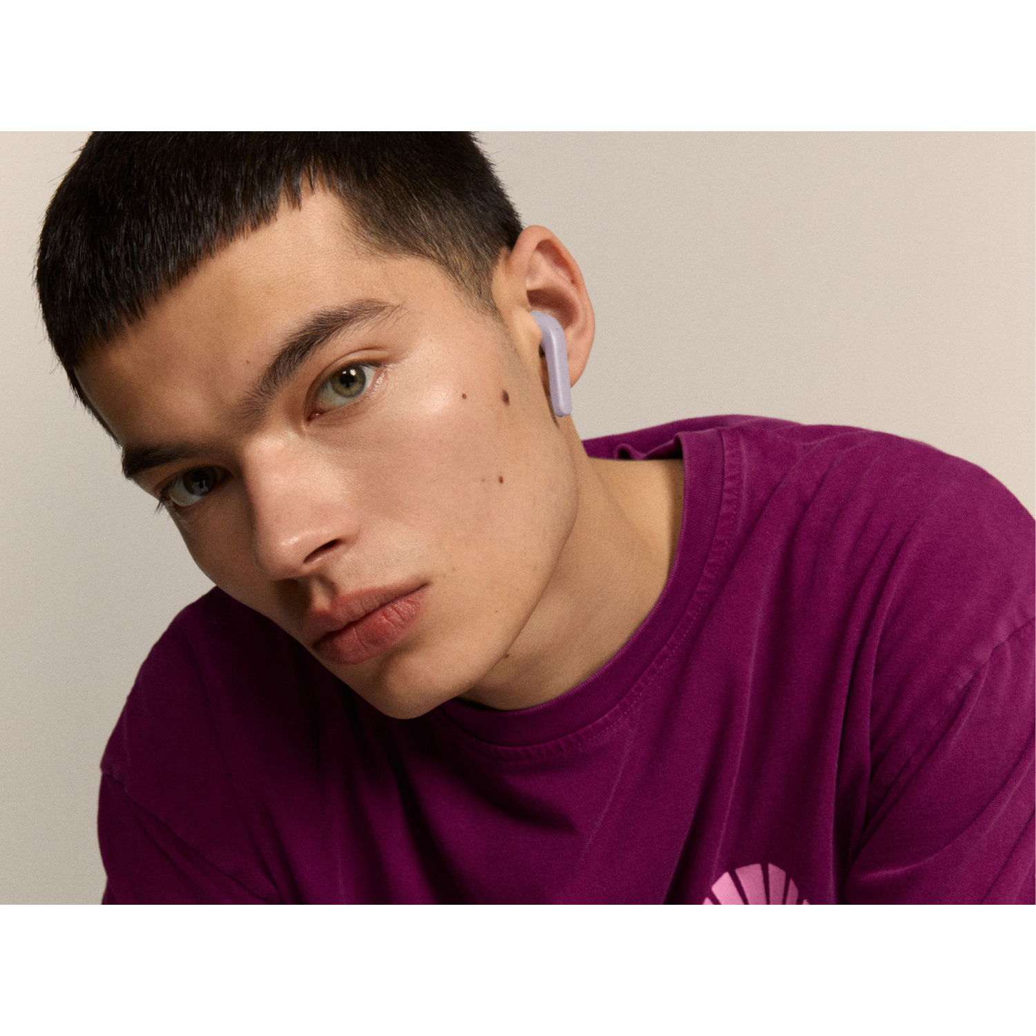 Un homme portant une chemise violette avec un écouteur lavande. Le fond est neutre.