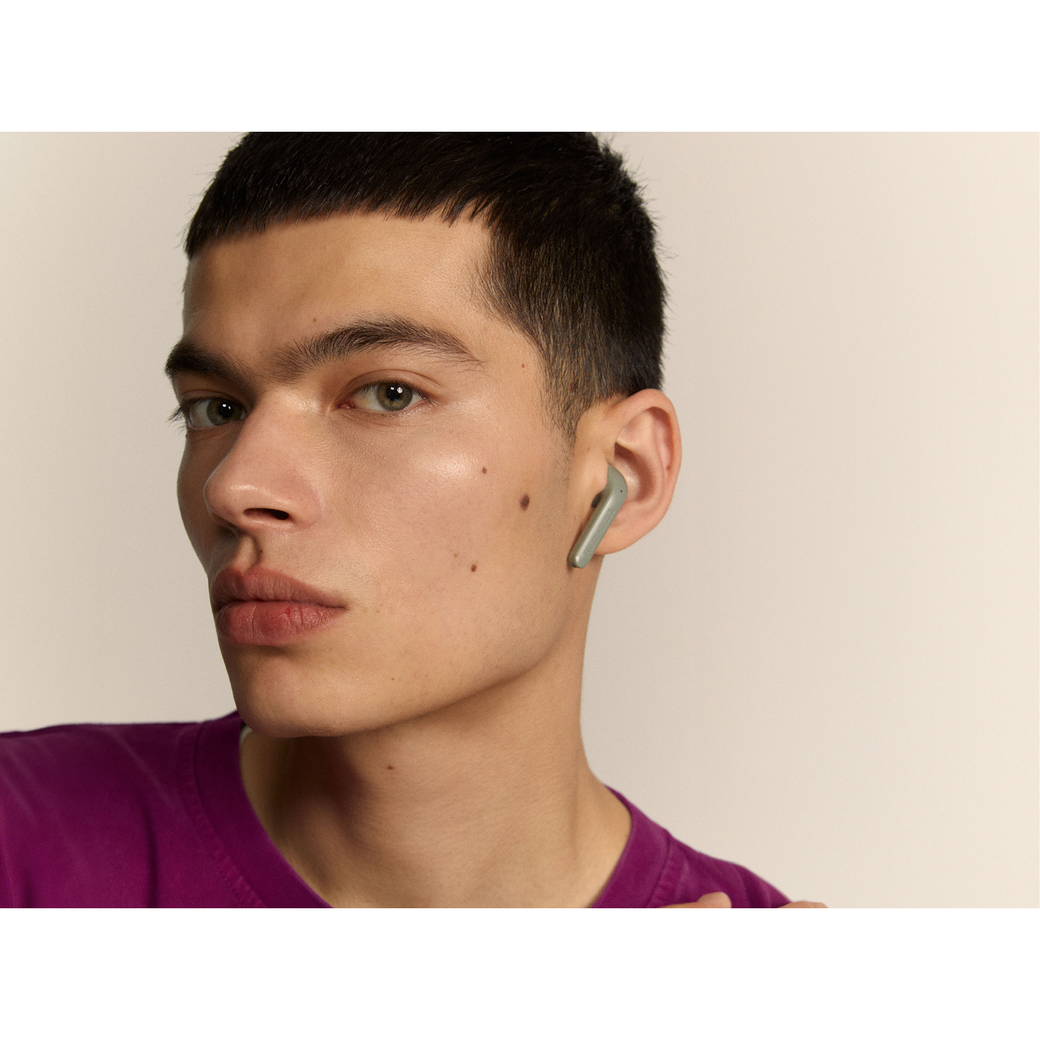 A man with a purple shirt wearing a green earbud in one ear.