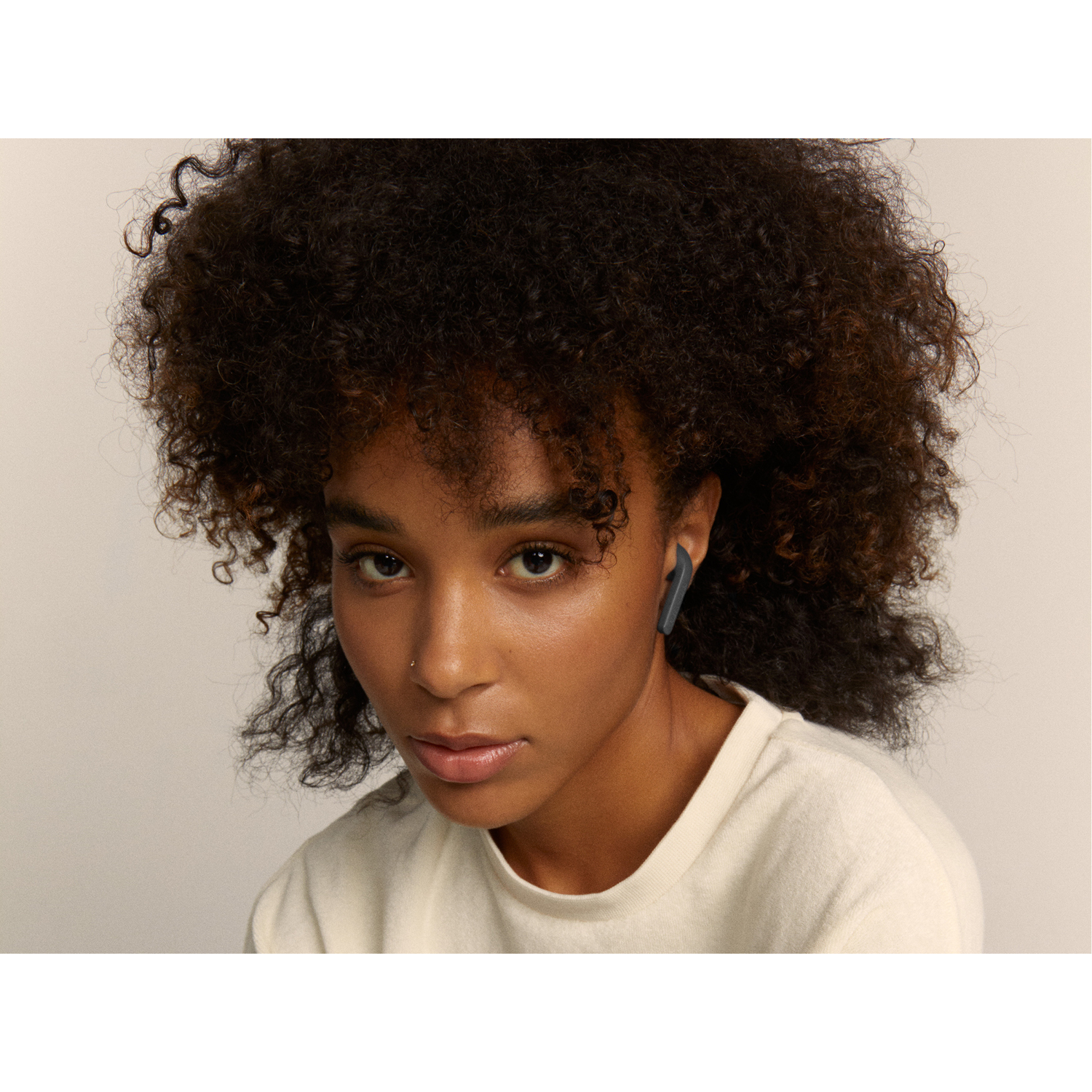 A woman with dark curly hair wearing an earbud in her ear.