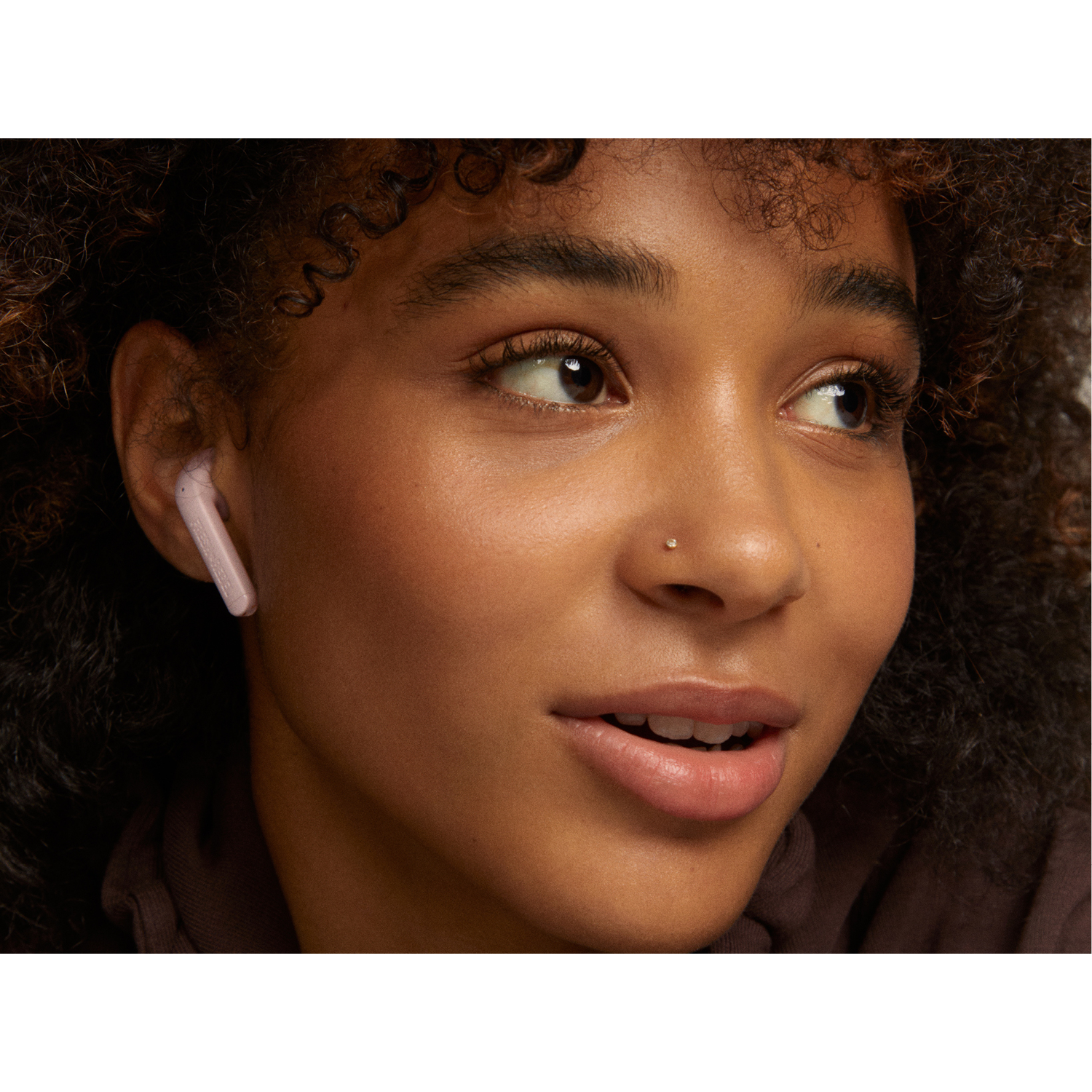 Close-up of woman with brown hair wearing pink earbuds, looking right.