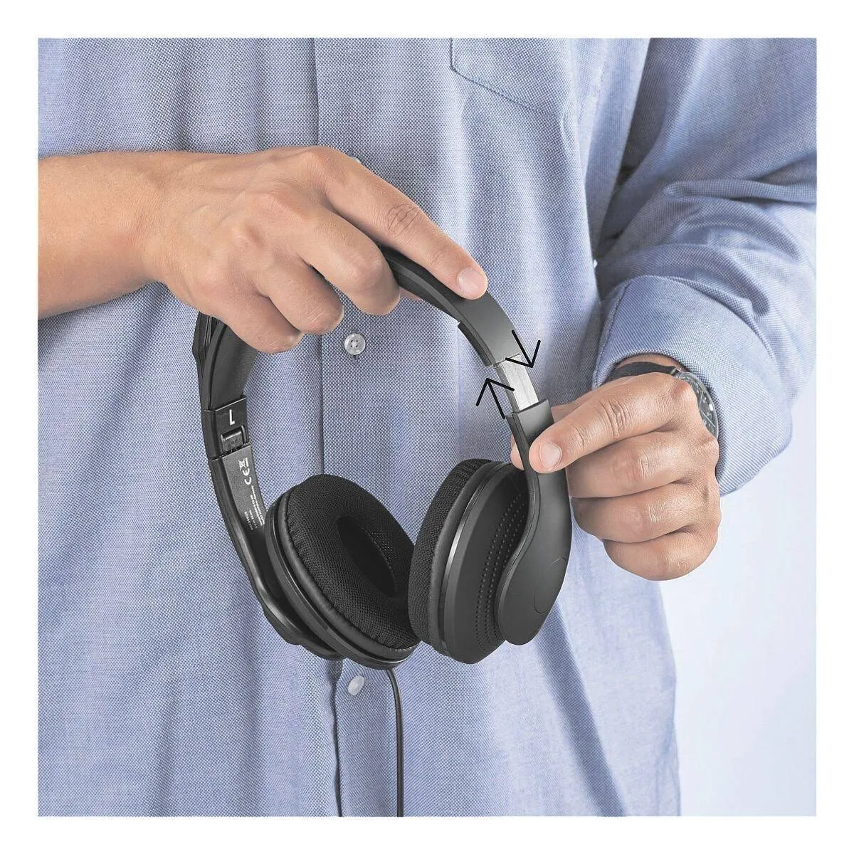 Un hombre sosteniendo auriculares negros. Sus manos están cerca de la banda ajustable de los auriculares.