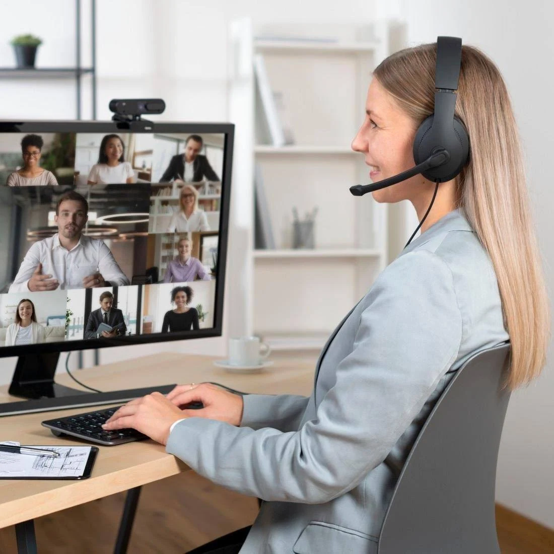 Una mujer con auriculares está en una videollamada. La pantalla muestra varios participantes.