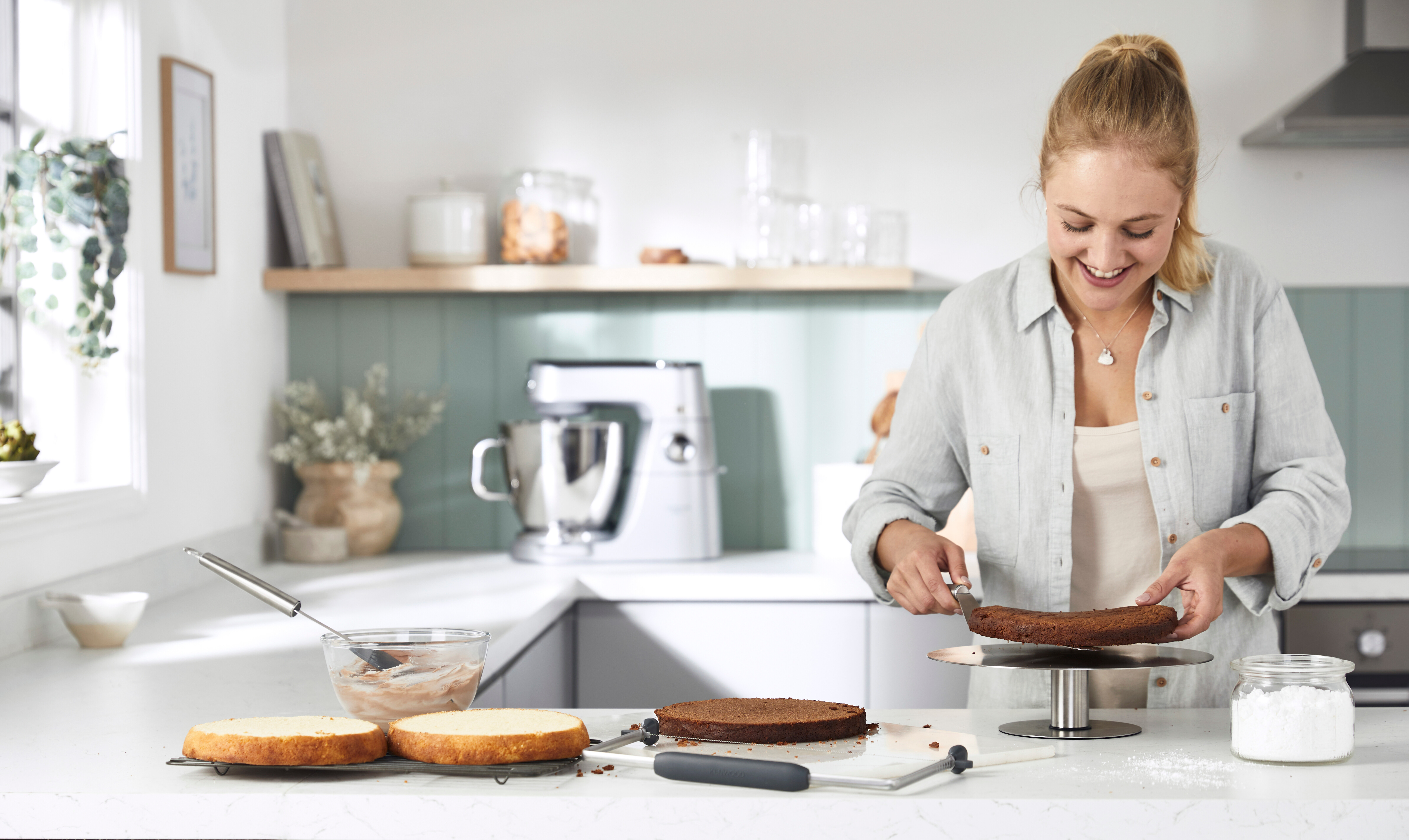 Eine Frau dekoriert einen Kuchen in einer modernen Küche. Backzutaten und Utensilien sind sichtbar.