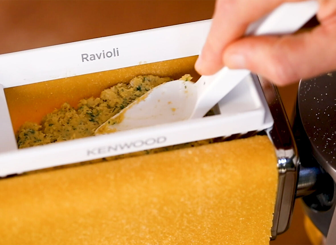 Ravioli-Maschine in Gebrauch. Befüllen von Ravioli mit einer Füllung mit einem weißen Löffel.