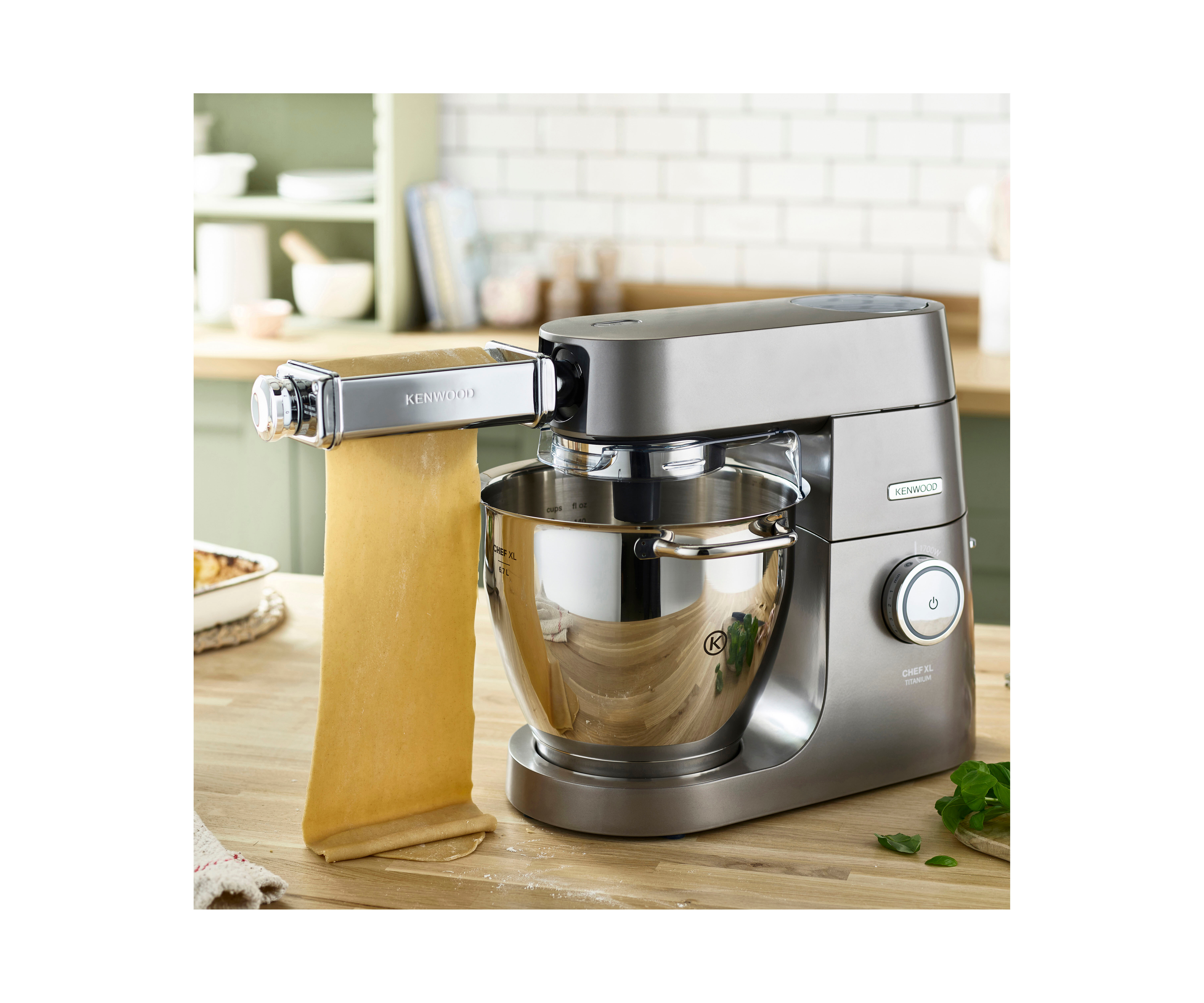 Ein Kenwood-Küchenmixer mit einem Nudelroller. Die Maschine ist grau und hat eine silberne Schüssel.