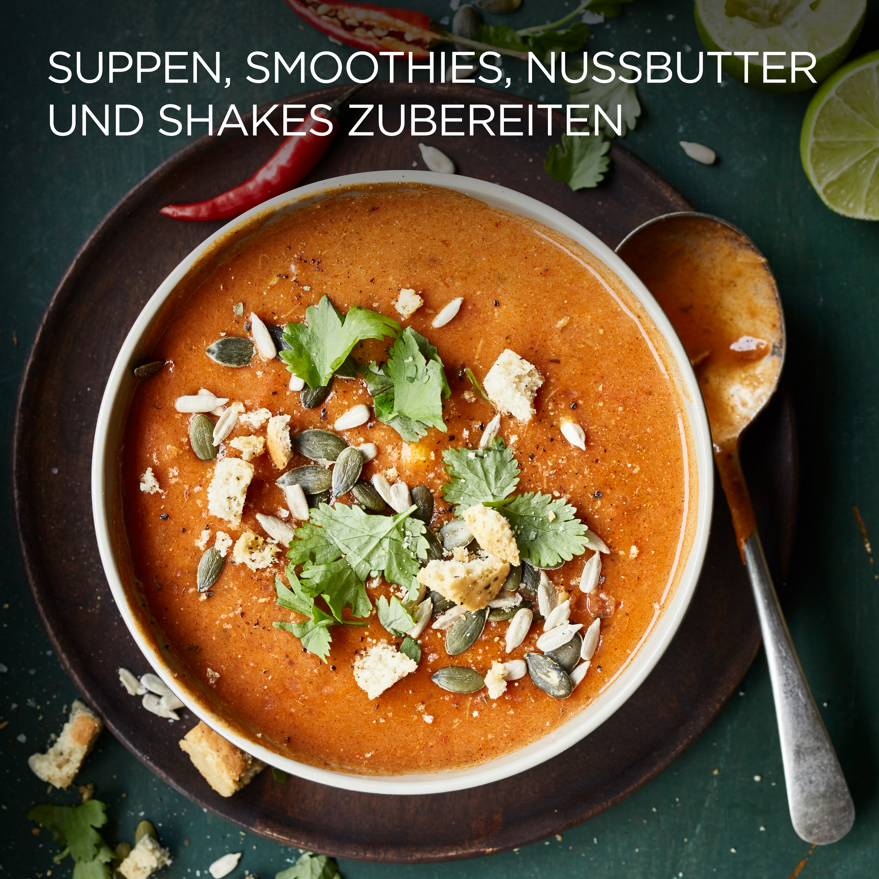 Eine Schüssel mit orangefarbener Suppe mit Garnierungen, neben Löffel und Limette.