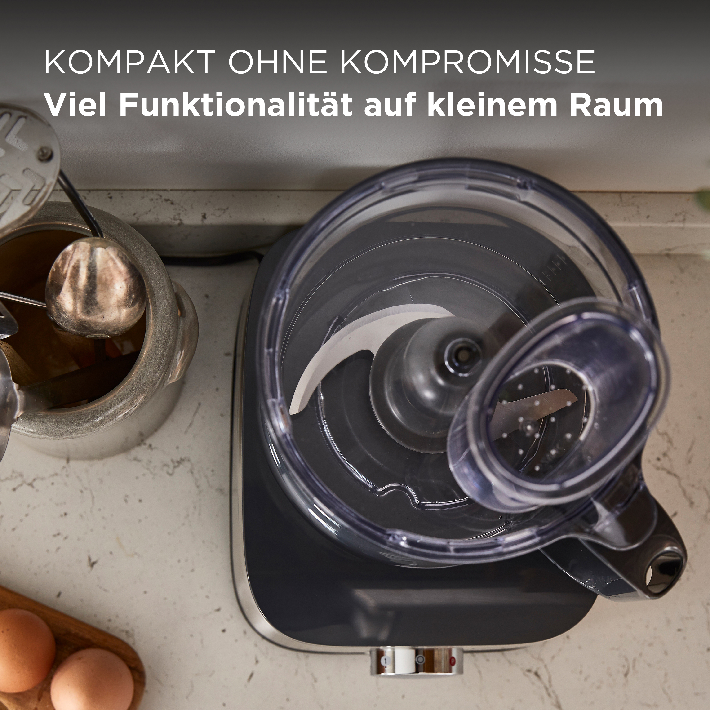 Küchenmaschine mit transparentem Behälter und Klinge. Text oben: kompakt, Funktionalität.