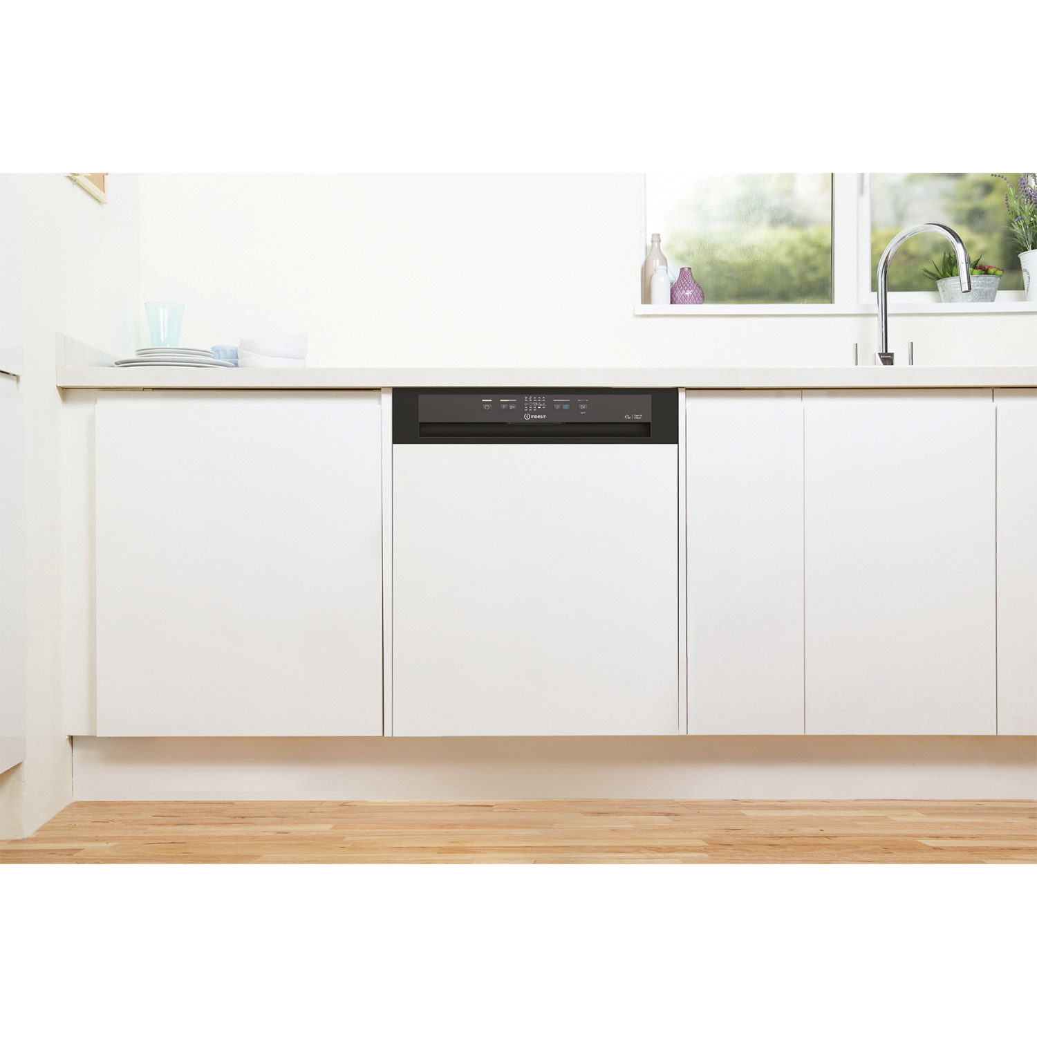 Lavastoviglie installata in cucina. Porta chiusa con pannello di controllo. Armadi bianchi, pavimento in legno.