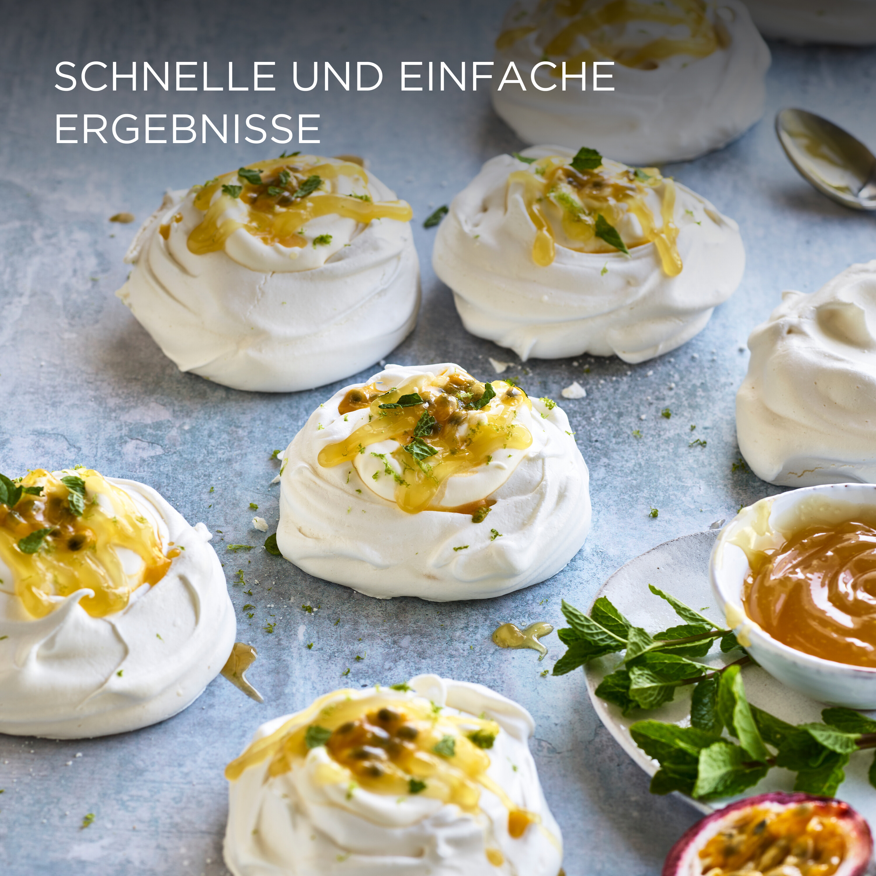 Pavlova-Desserts mit Passionsfrucht und Minze, serviert auf einer hellblauen Oberfläche.