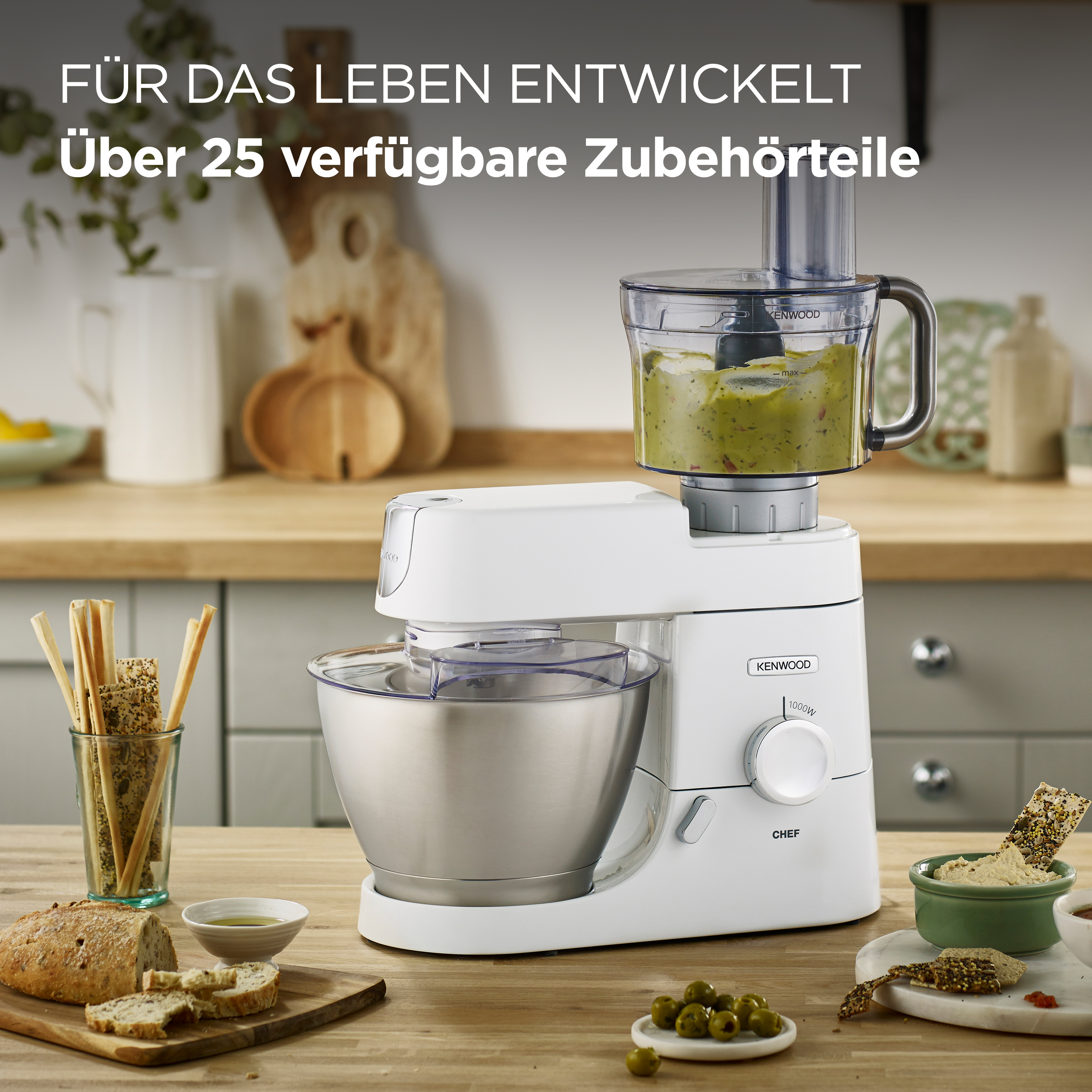 Weißer Küchenroboter mit Zutaten. Brot, Oliven und Gemüse sind sichtbar.