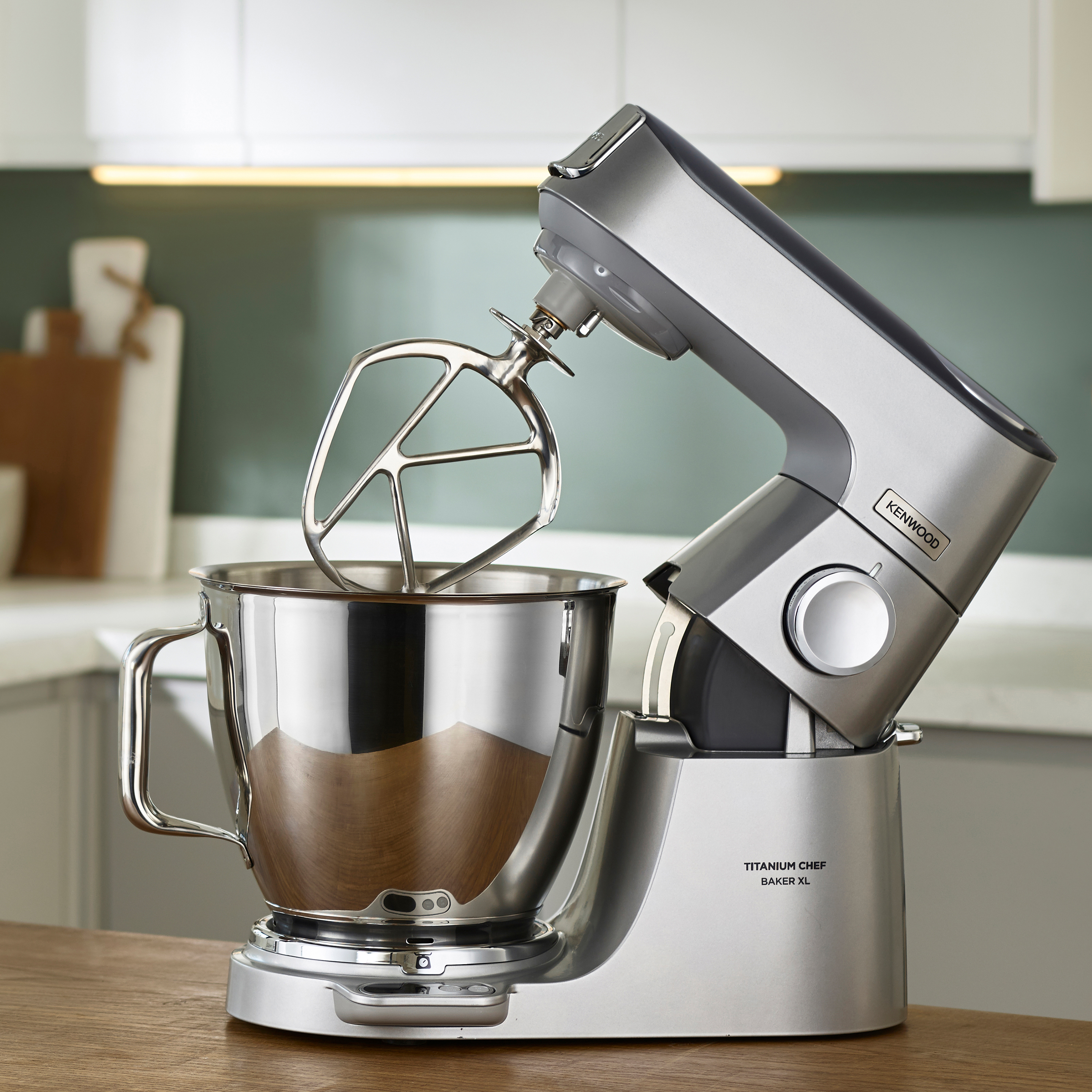 Silberner Kenwood Mixer mit Schüssel, Schneebesen und hölzerner Arbeitsplatte.
