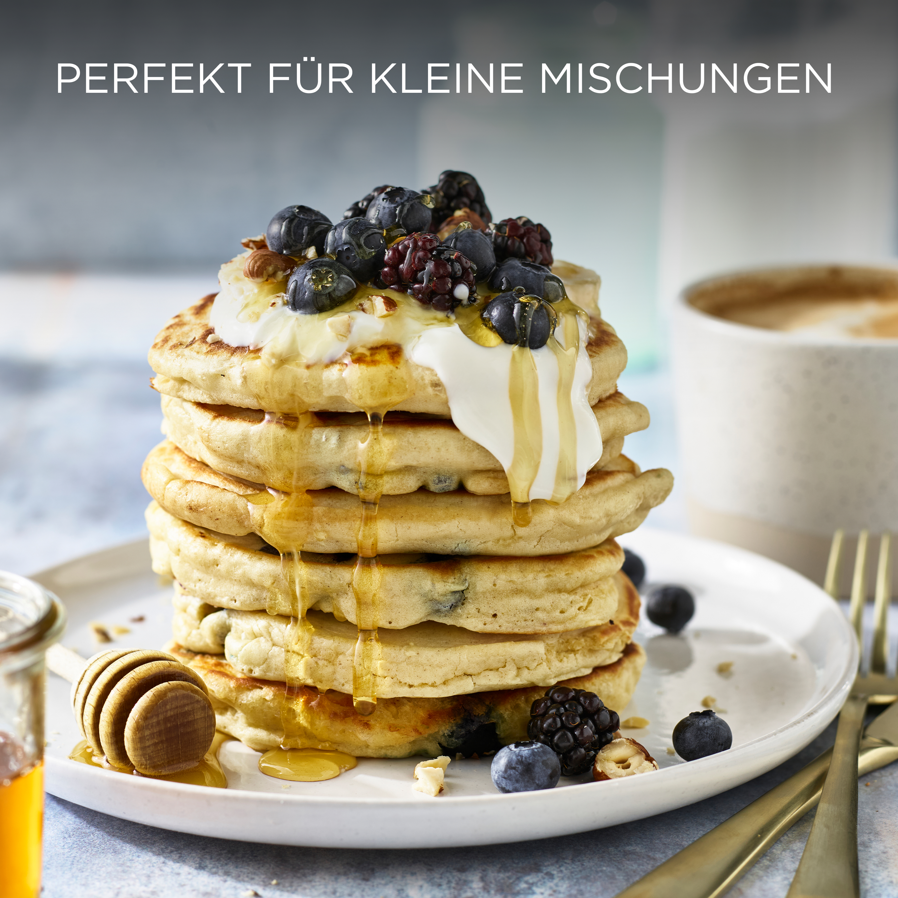 Pfannkuchen mit Toppings, darunter Blaubeeren und Honig. Eine Tasse Kaffee ist in der Nähe.