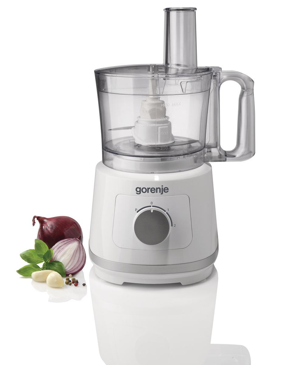 Eine weiße Küchenmaschine mit Zutaten wie Zwiebeln, Knoblauch und Basilikum auf weißer Oberfläche.