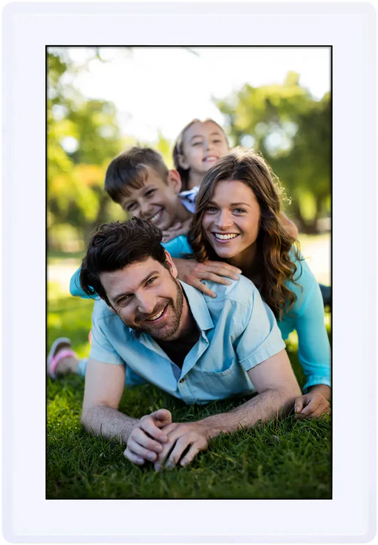 Famille de quatre souriant sur l'herbe, avec un parc vert en arrière-plan.