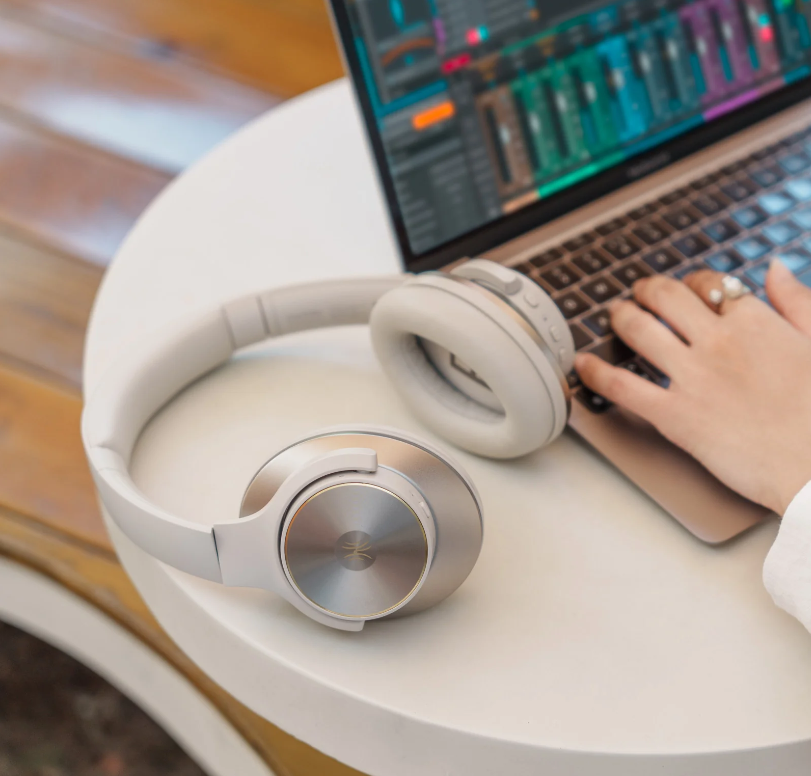 Kopfhörer auf einem weißen Tisch mit geöffnetem Laptop und Hand auf dem Trackpad.