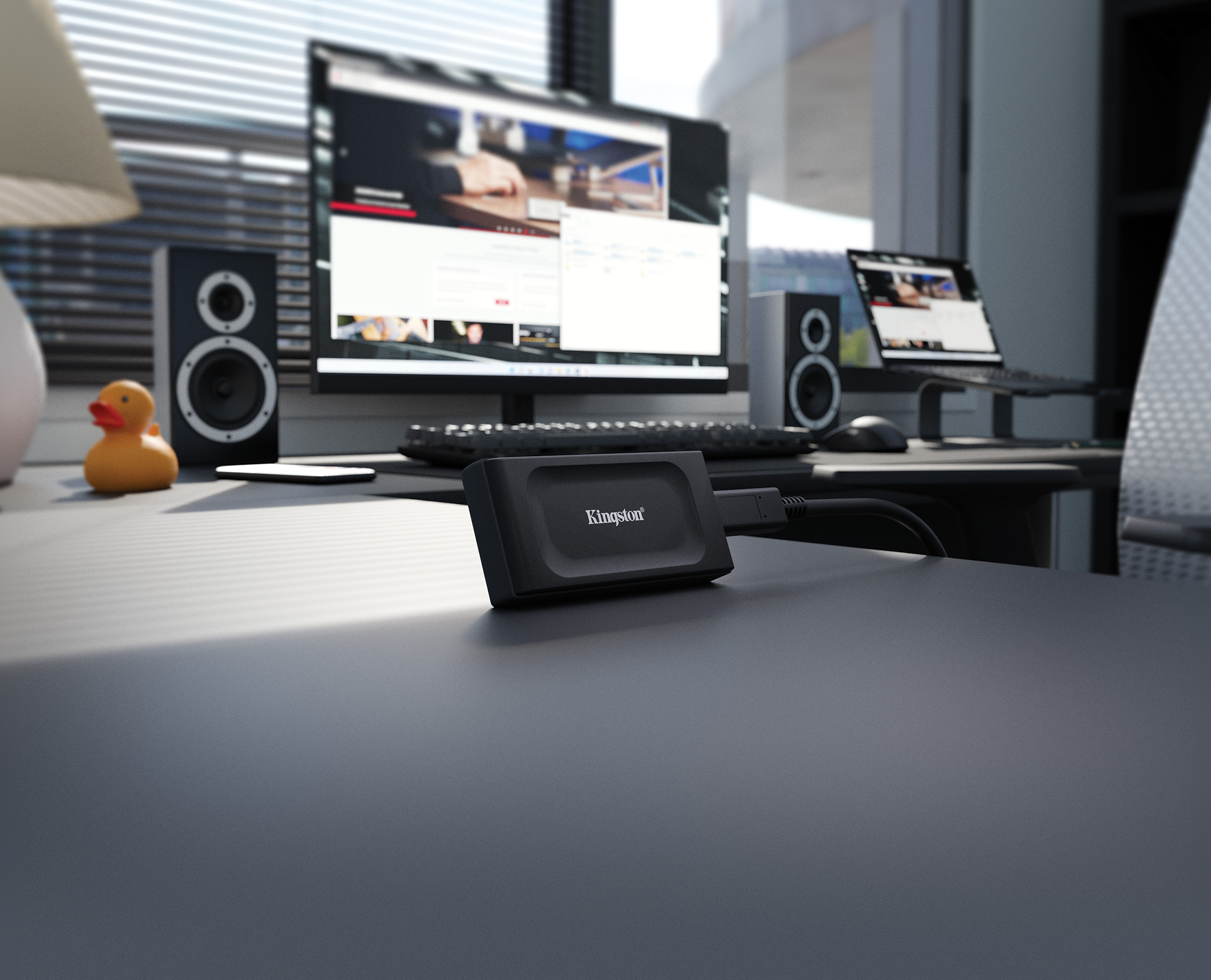 Schreibtisch mit Computer, Lautsprechern, Laptop, Ente und Kingston-Festplatte.