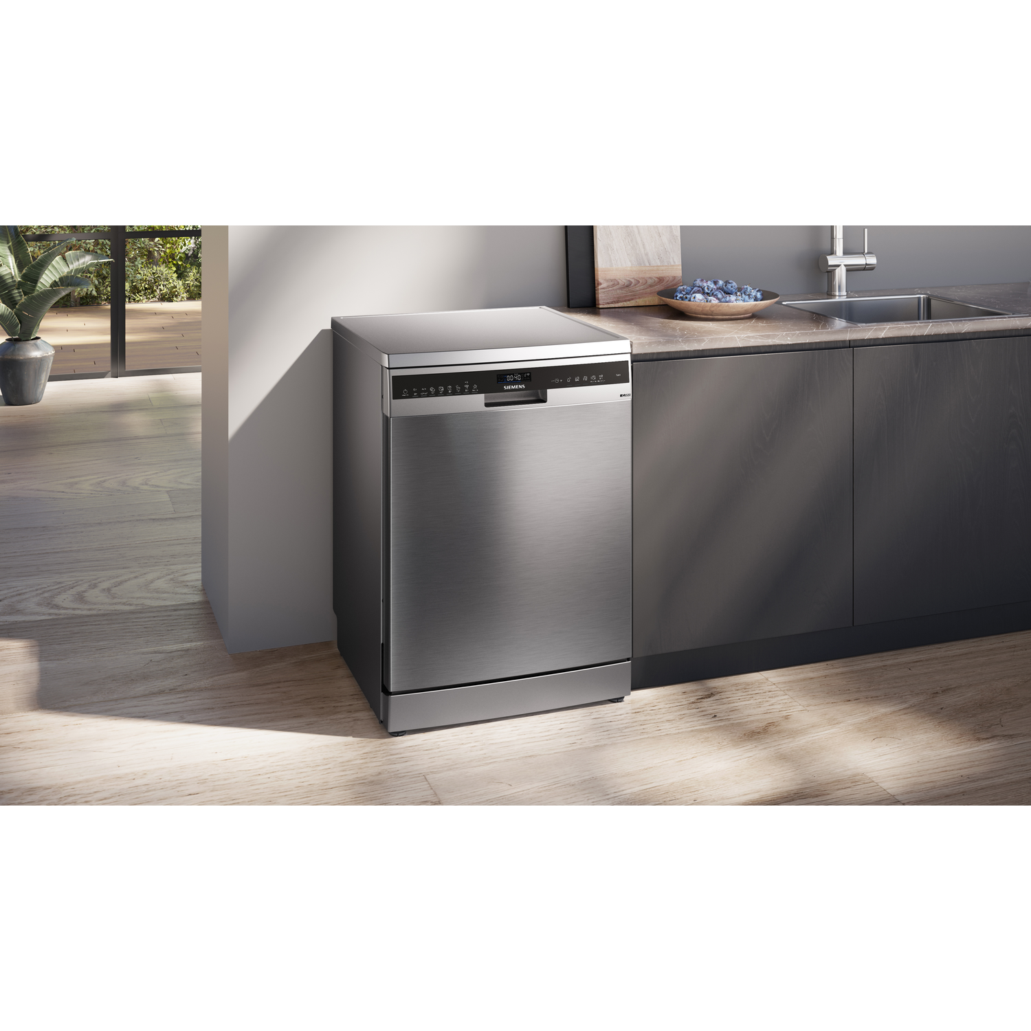 A silver dishwasher standing in a kitchen with wooden floors and cabinets.