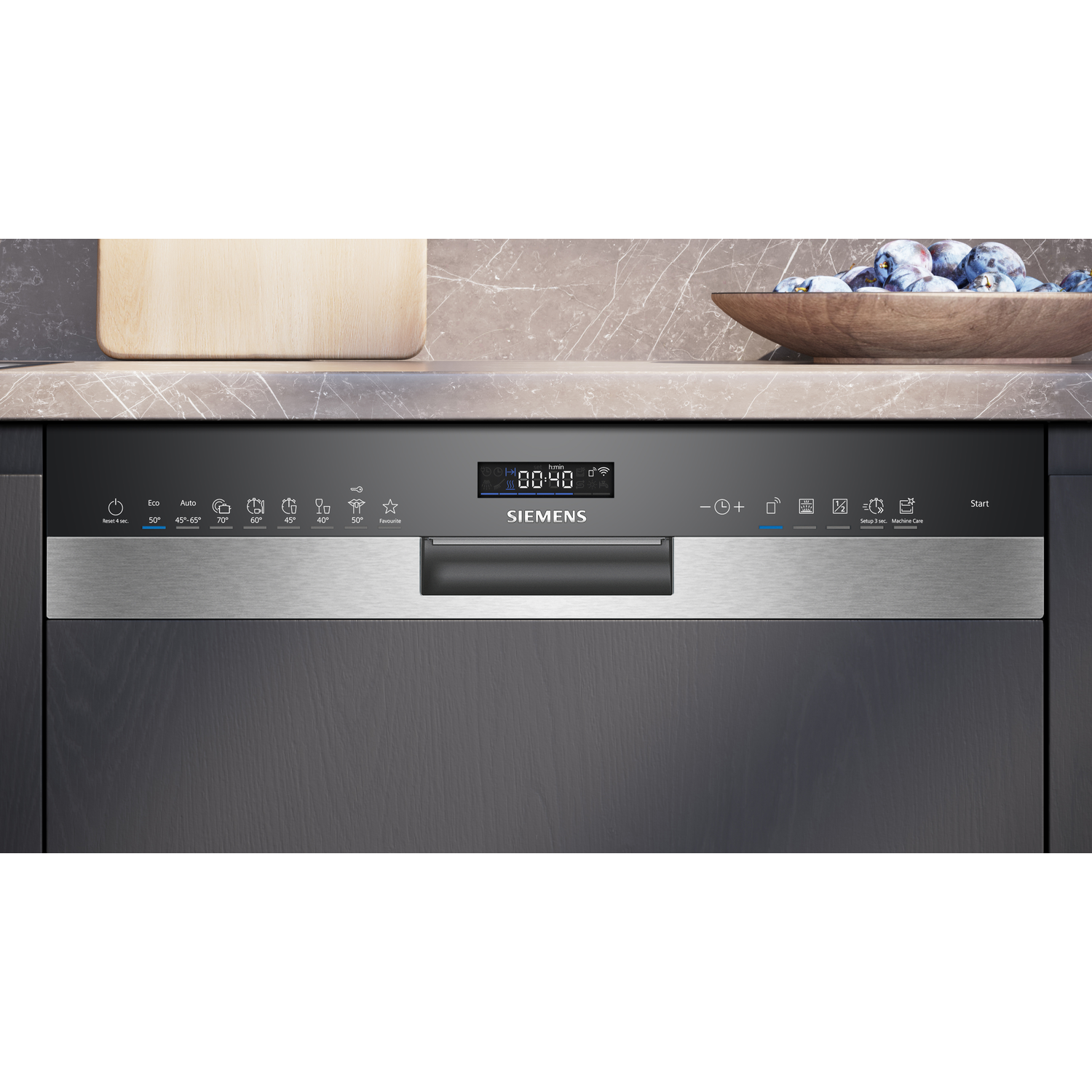 Vaatwasser bedieningspaneel met digitaal display, knoppen en roestvrijstalen handgreep. Een houten plank en kom pruimen op de achtergrond.