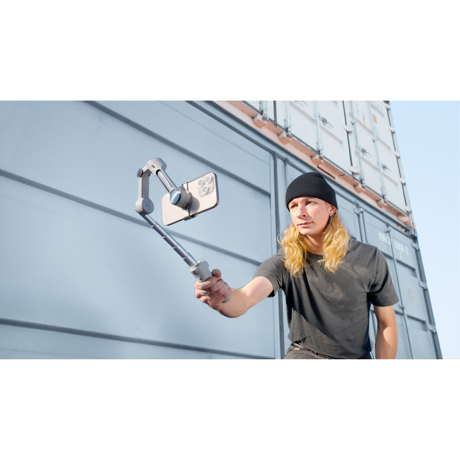 Man holding a phone on a gimbal in front of shipping containers.