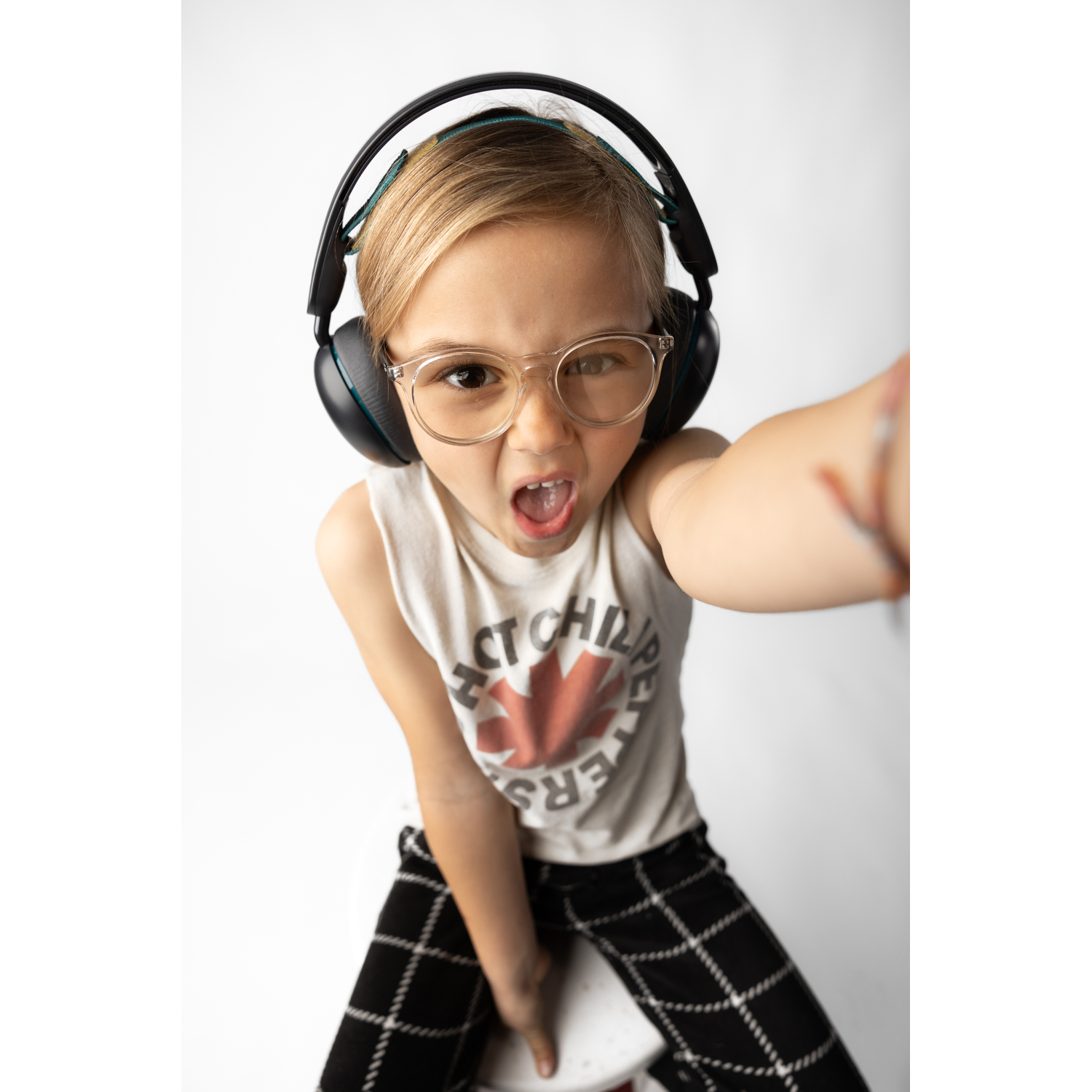 Blonde child with glasses and headphones making a face. White background.