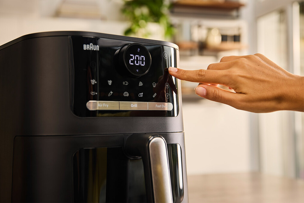 Friteuse à air noire avec affichage numérique et une main appuyant sur un bouton.