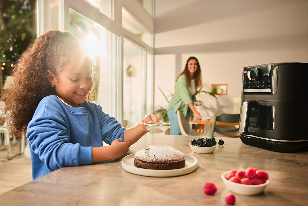 Enfant saupoudrant du sucre glace sur un gâteau, un parent à proximité.