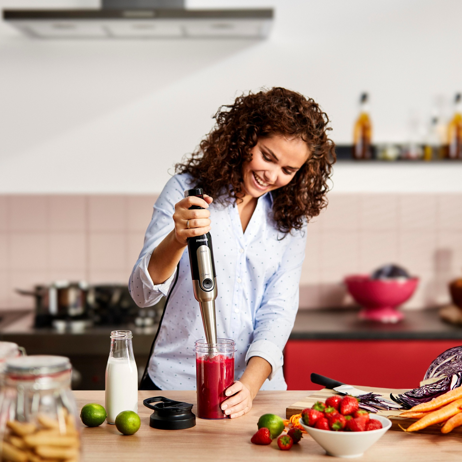 Donna che frulla frutta rossa in un bicchiere con un frullatore, ambiente cucina.