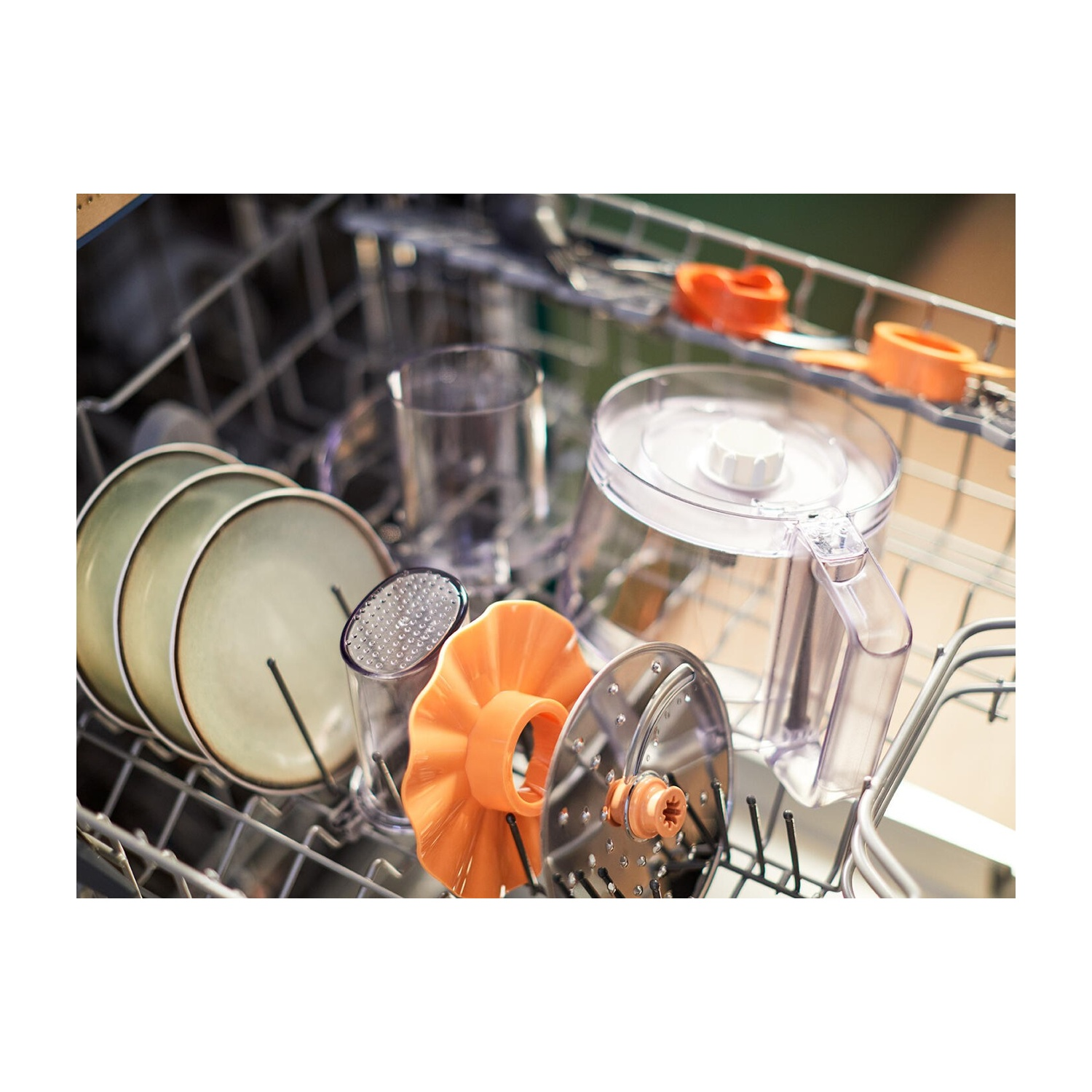 Lavastoviglie con piatti, bicchieri e parti di robot da cucina. Principalmente trasparente e arancione. All'interno di una lavastoviglie.