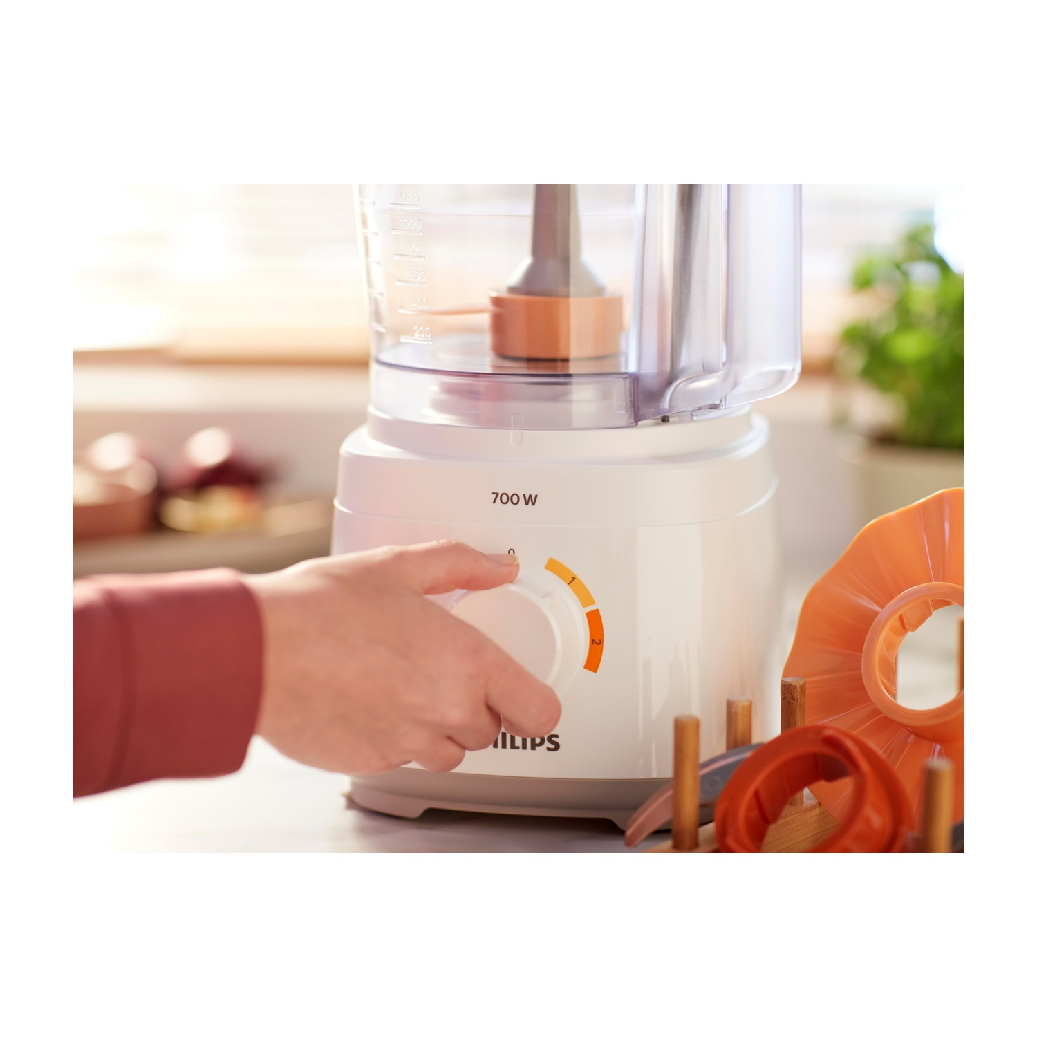 Robot da cucina bianco con una mano che gira una manopola. Altre parti sono visibili, come un disco da taglio e verdure.