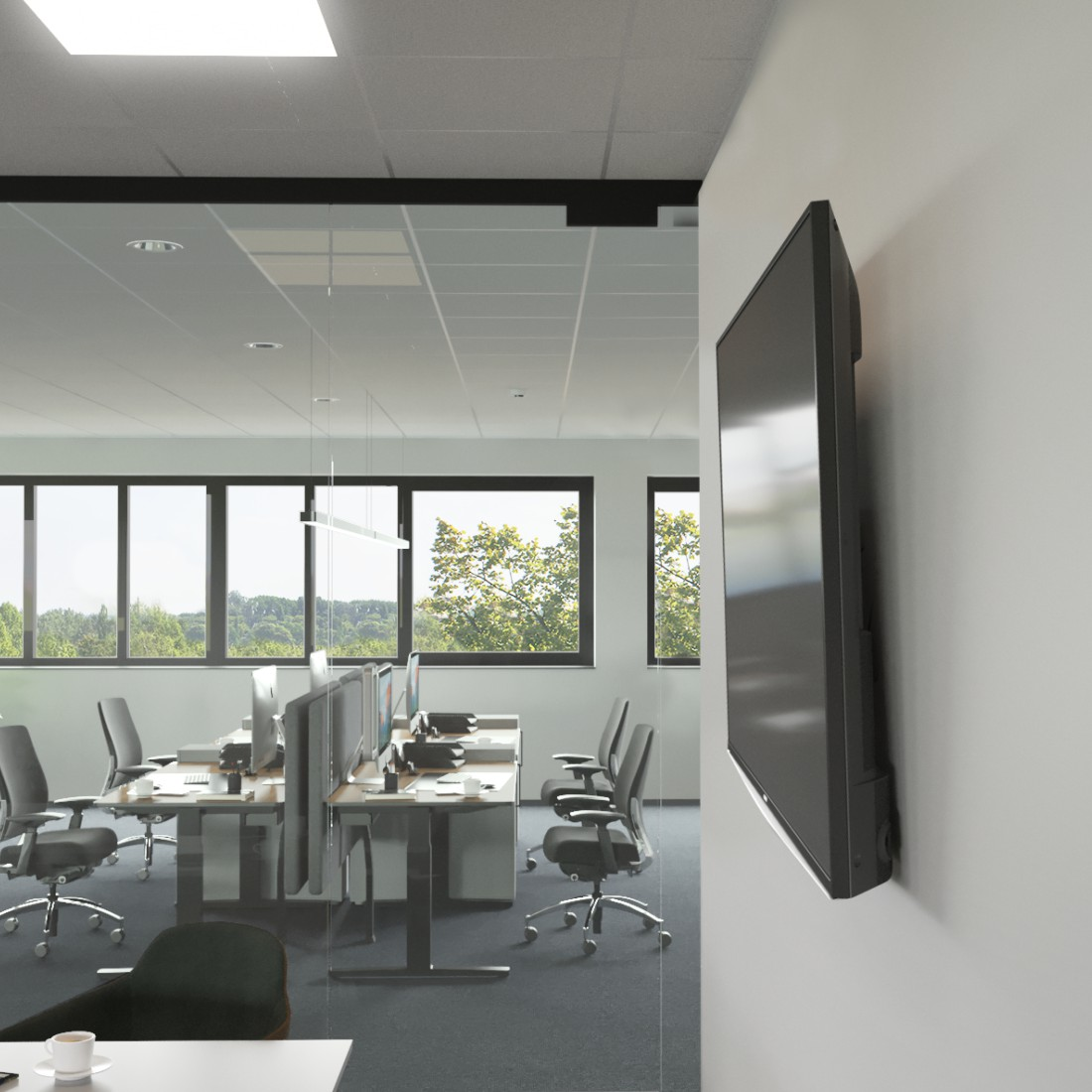 Fernseher an einer weißen Wand in einem Büroumfeld mit Schreibtischen und Fenstern.