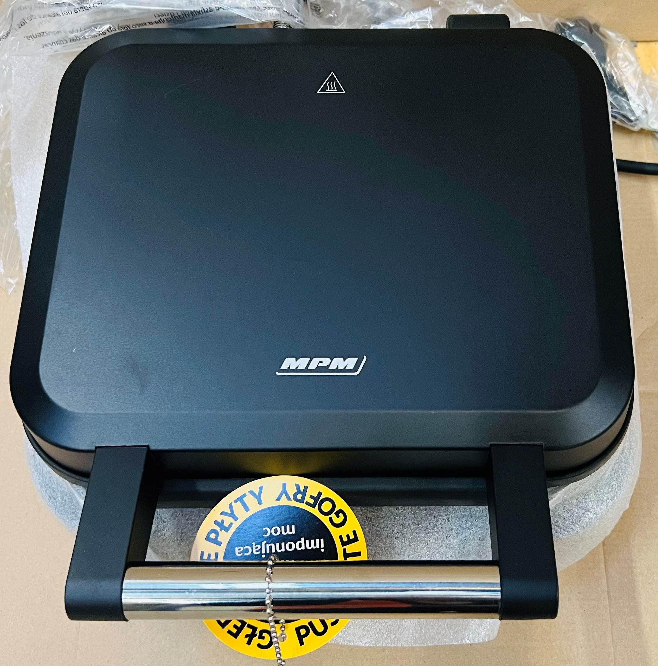 Czarny gofrownica na kartonie, z uchwytem i widocznym logo marki.