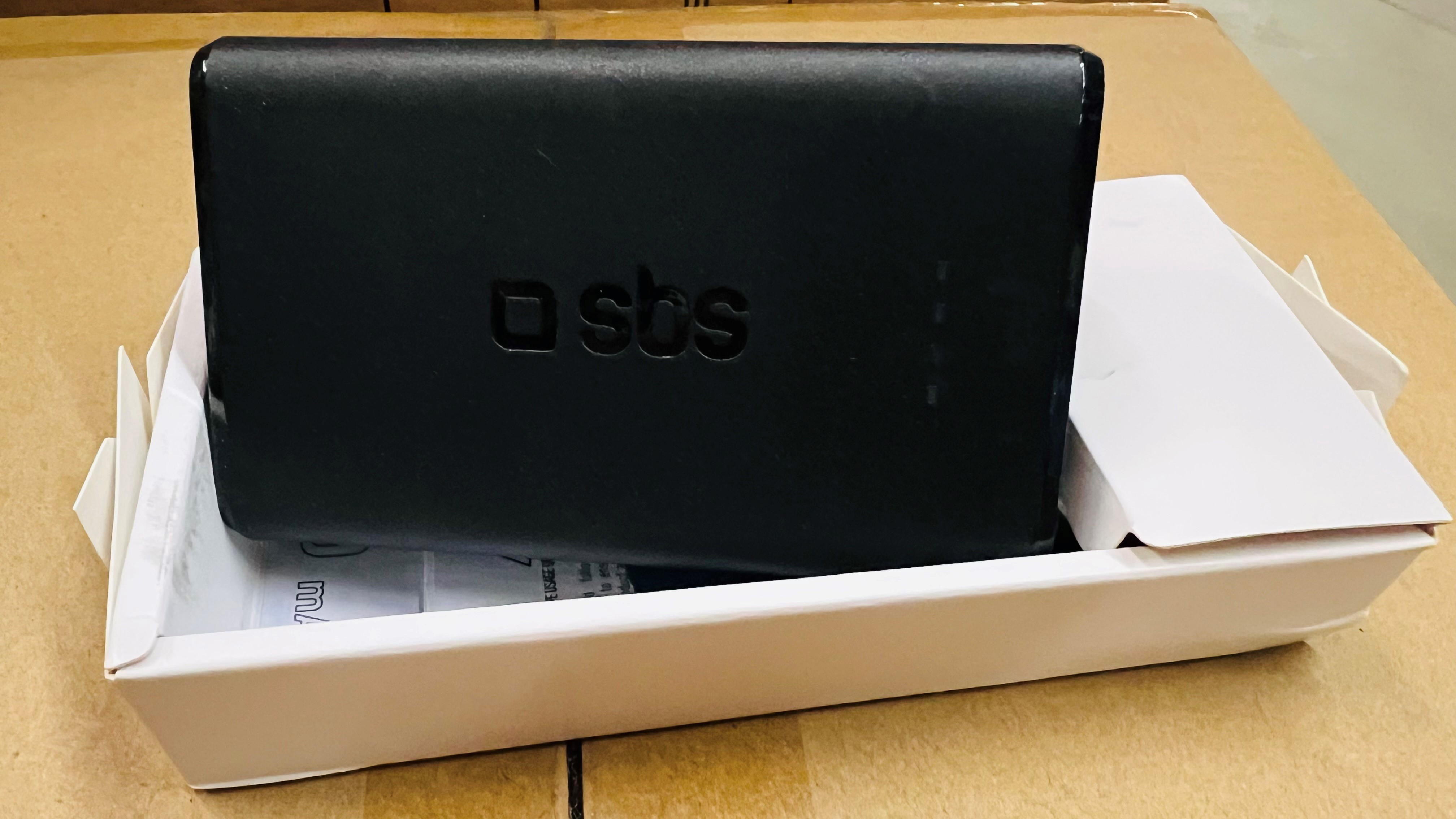 Czarny power bank SBS w białym pudełku na kartonowej powierzchni.