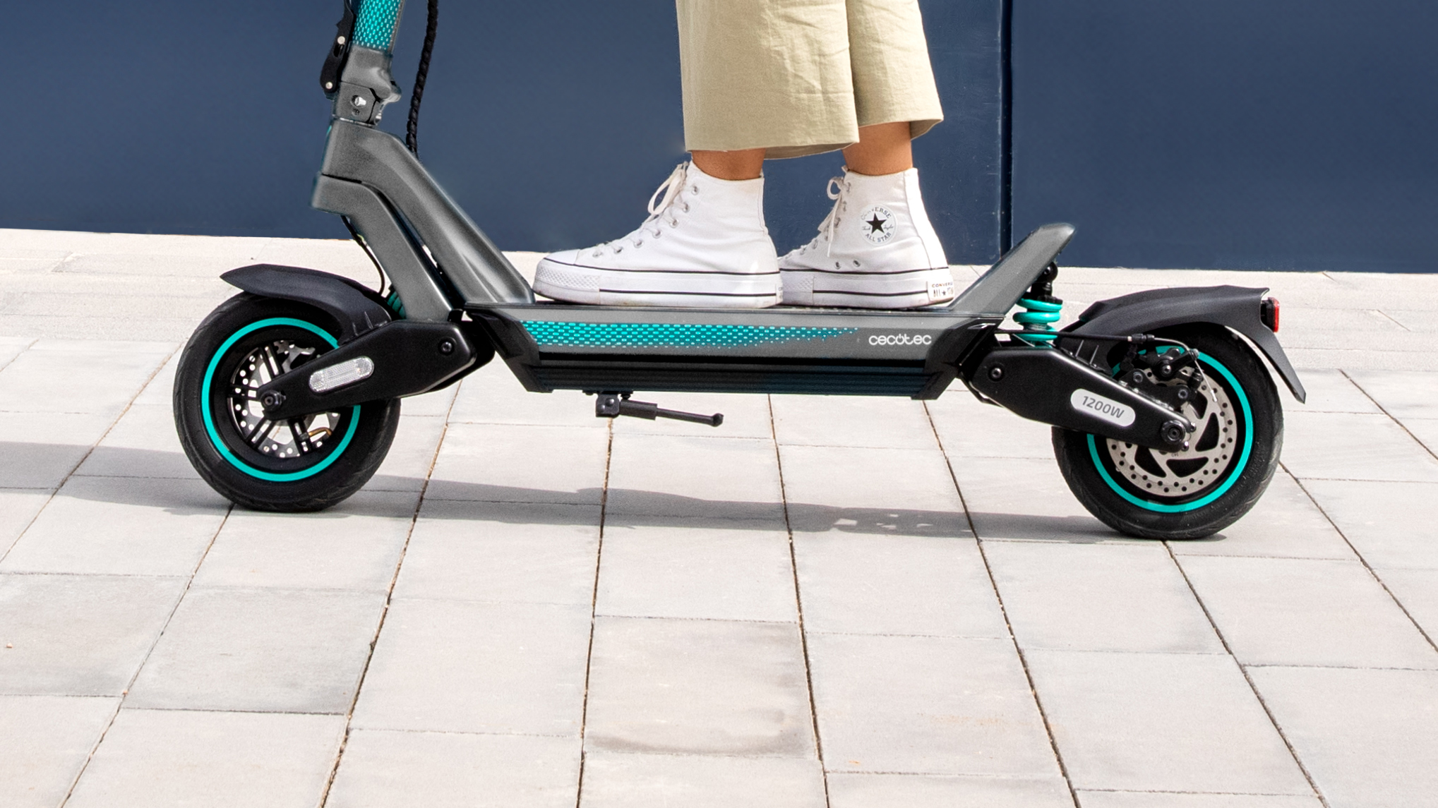 Una persona montando un patinete eléctrico en una acera gris, ángulo bajo.