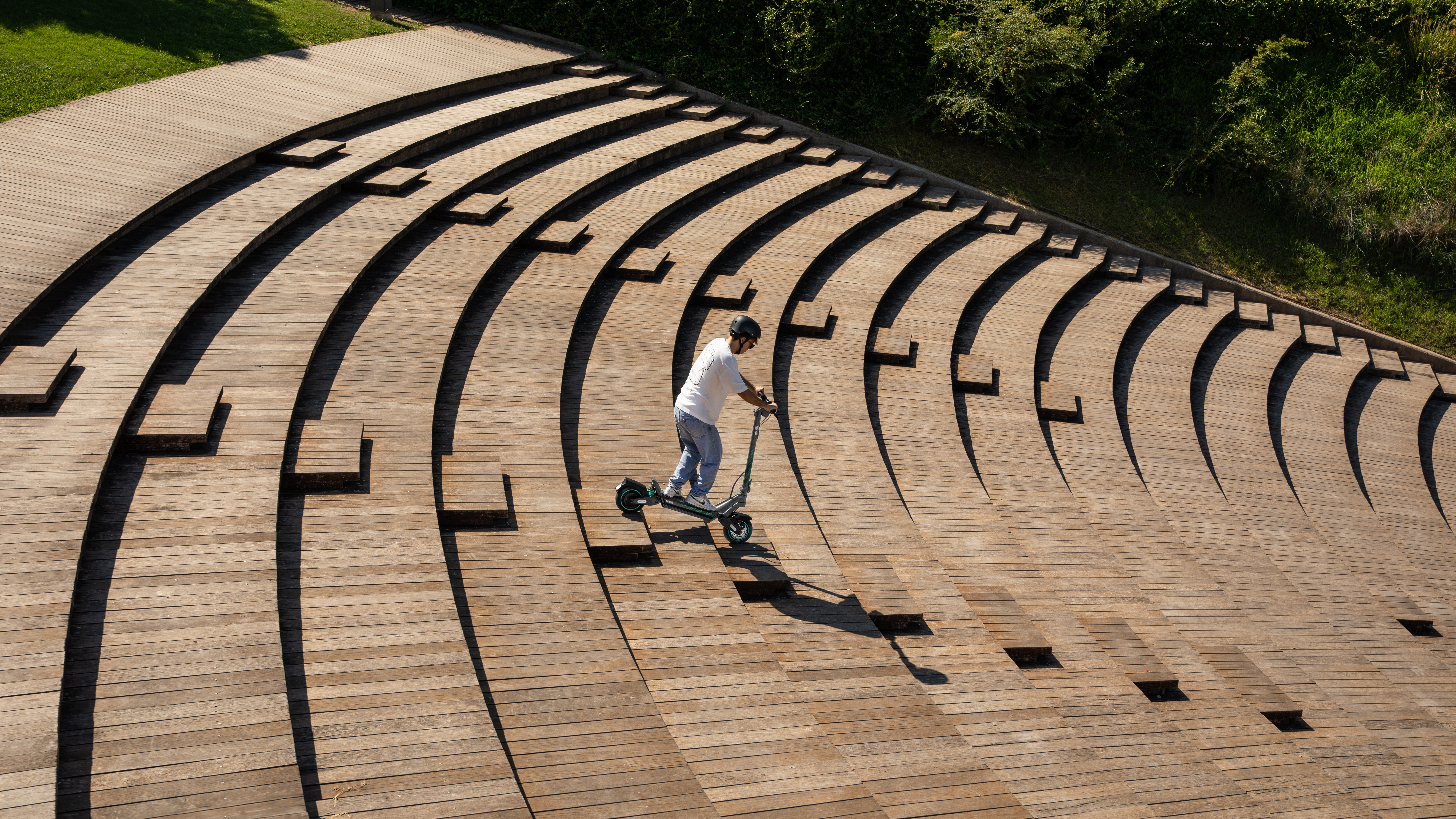 Un hombre monta un patinete eléctrico por escaleras de madera. Hay árboles en el fondo.