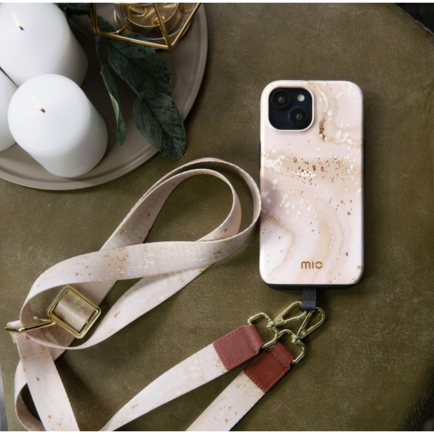 A phone in a marbled case with a strap lying on a green surface. Candles are in the background.