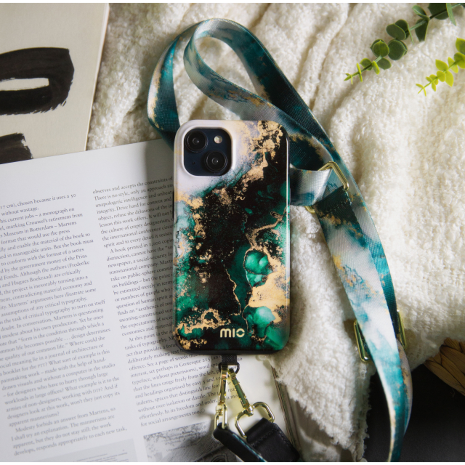 Phone case with a green and gold design, with a phone and a strap on a desk with text and a book.