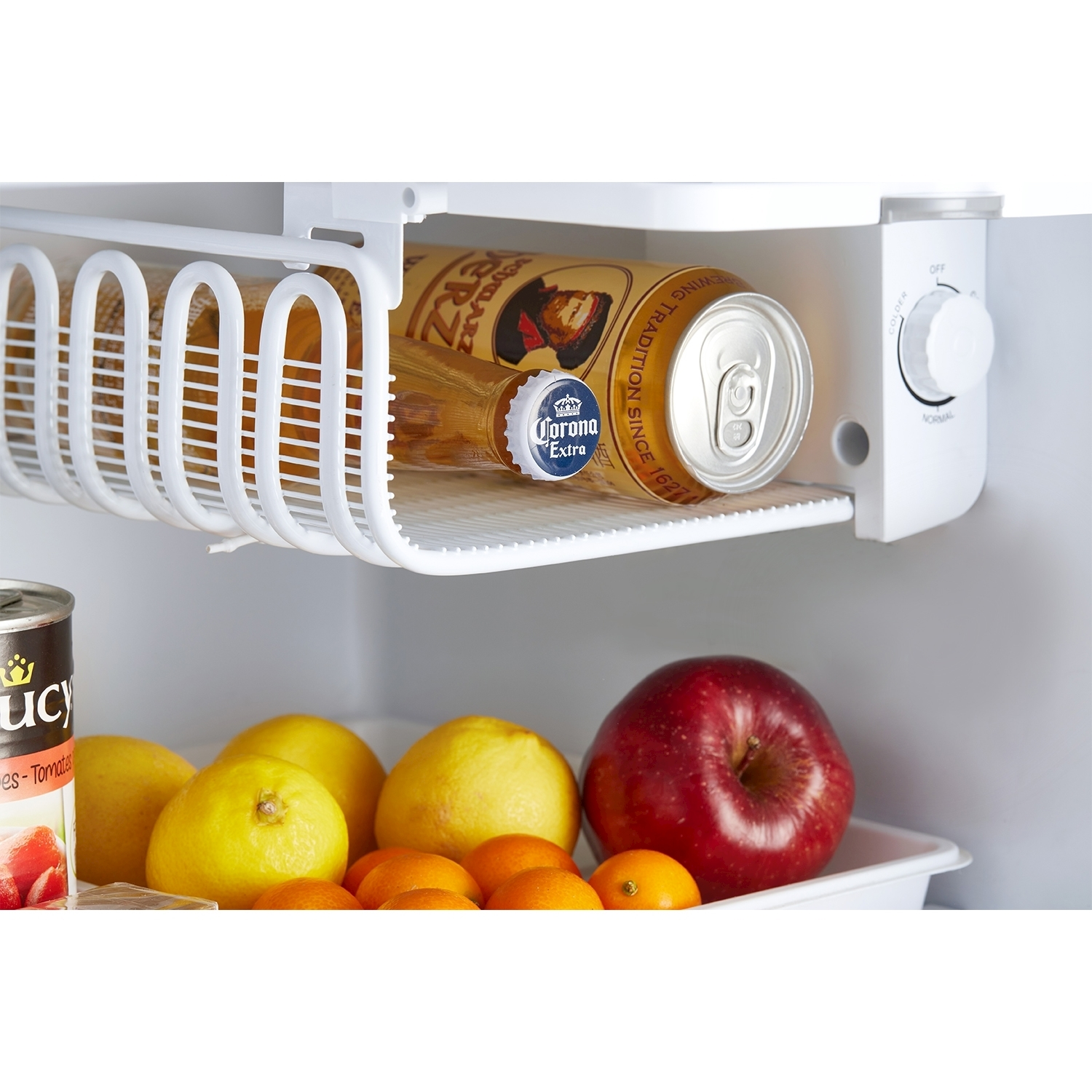 Interno del frigorifero con frutta e una lattina di soda. Un ripiano bianco contiene oggetti.