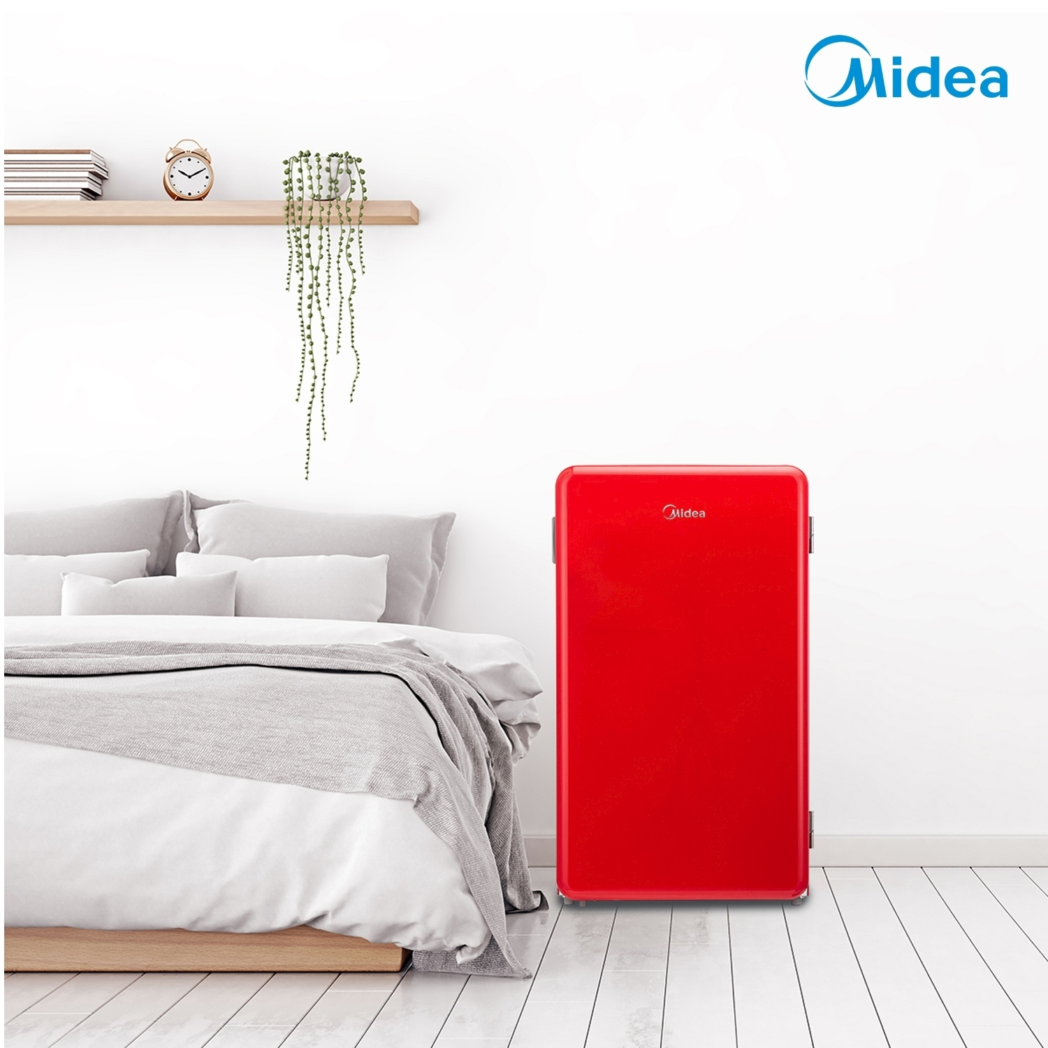 Frigorifero Midea rosso accanto a un letto, sfondo bianco con pianta.