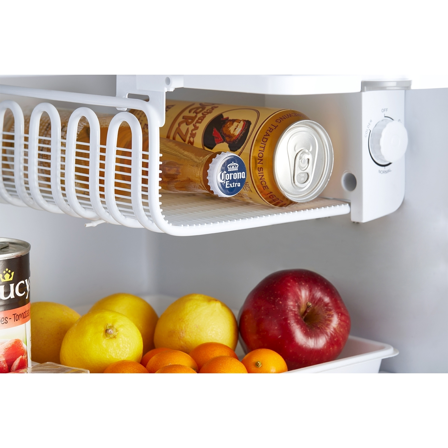 Interno di un mini frigo con cibo: limoni, arance, mele e una lattina di birra.