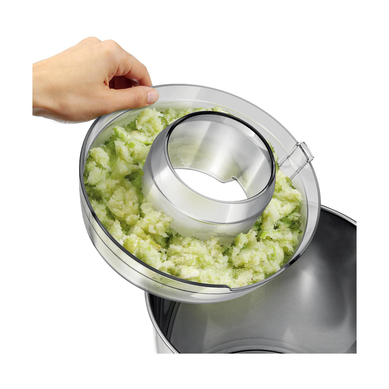 Una mano tiene un coperchio con verdure tritate sopra un robot da cucina.