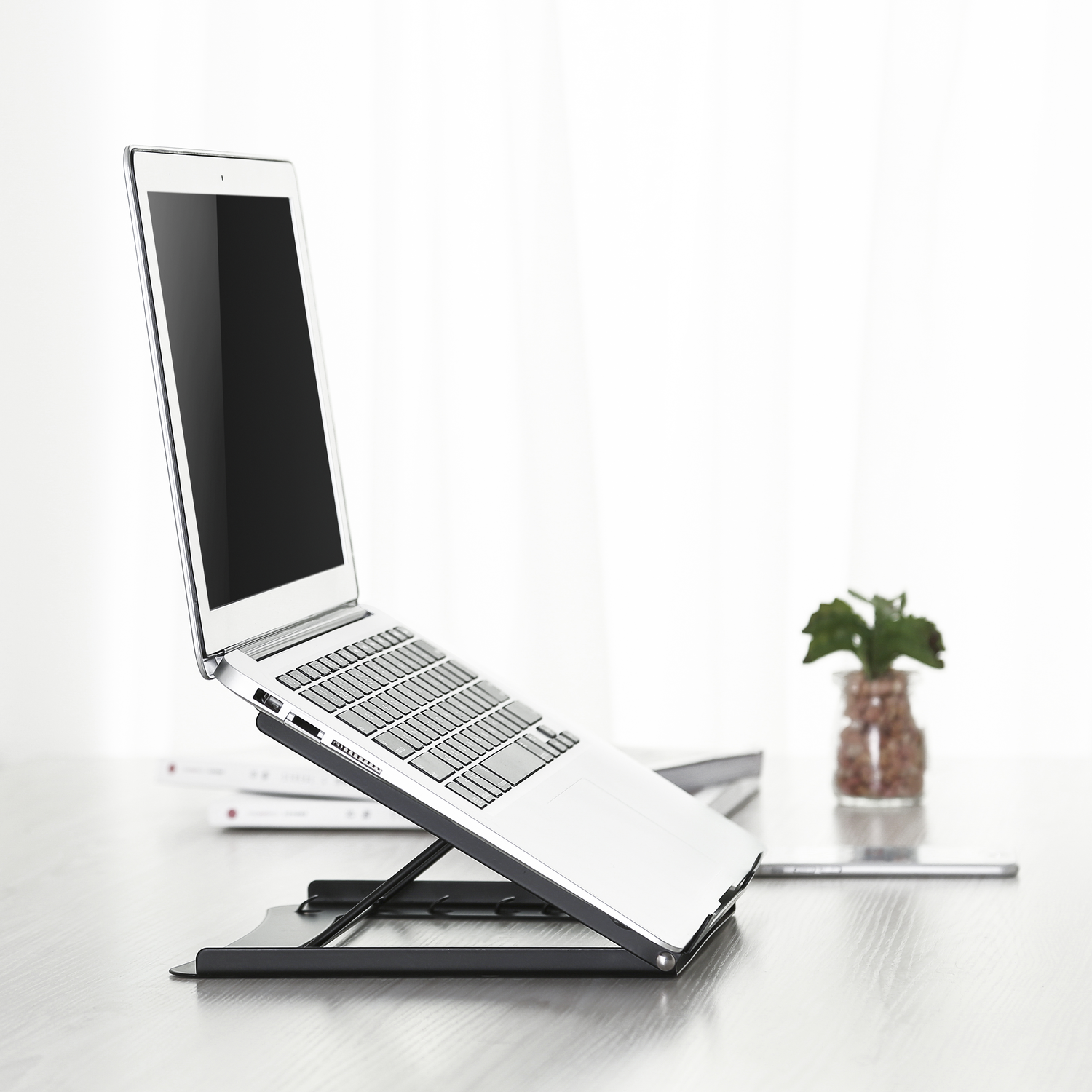 Laptop on a stand on a desk, with a glass jar and plant.